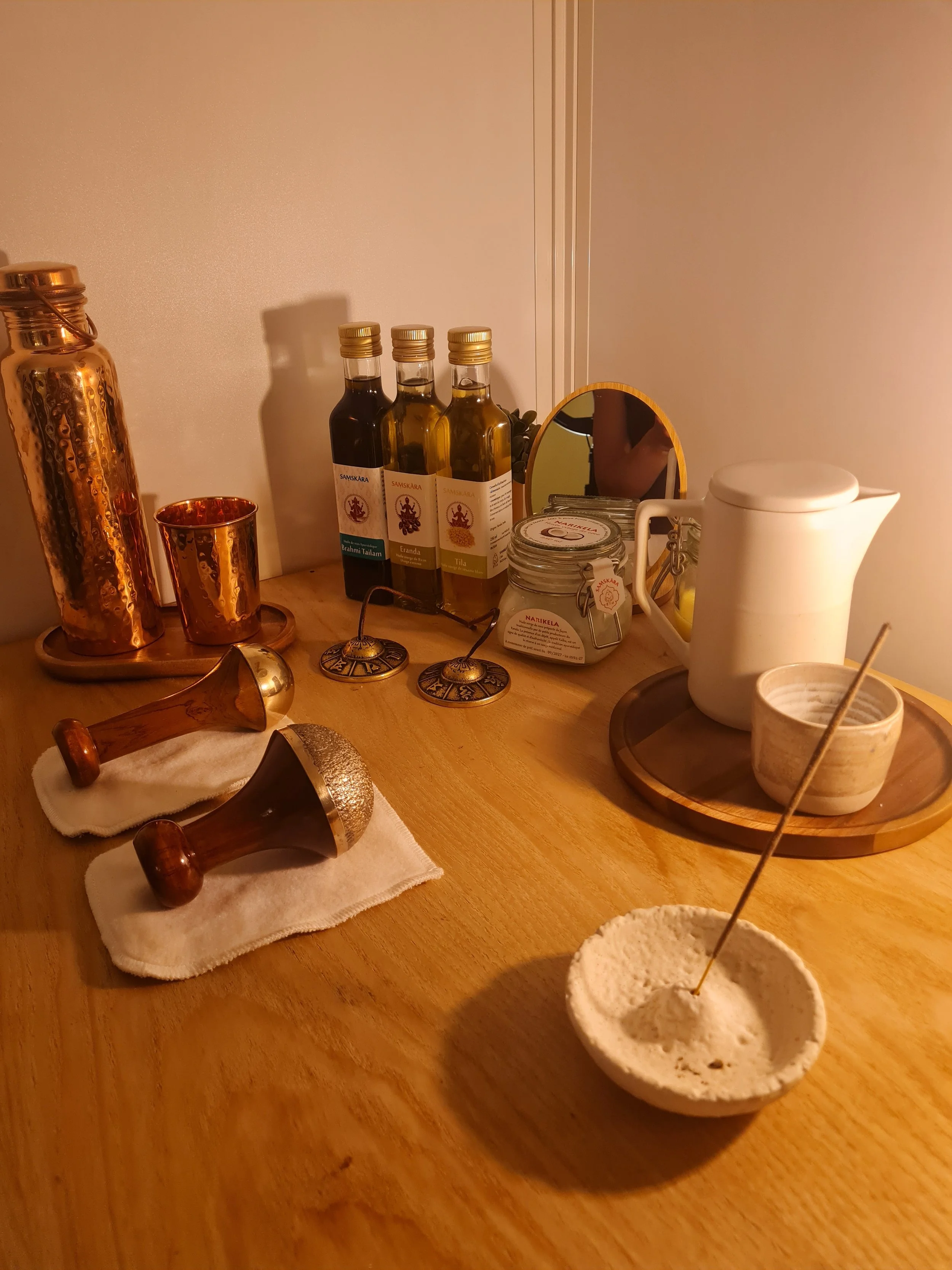 Table de thé avec divers récipients en métal, bouteilles d'huiles essentielles, petite trousse en tissu blanche, accessoires de massage, et une petite boule de pâte à modeler.