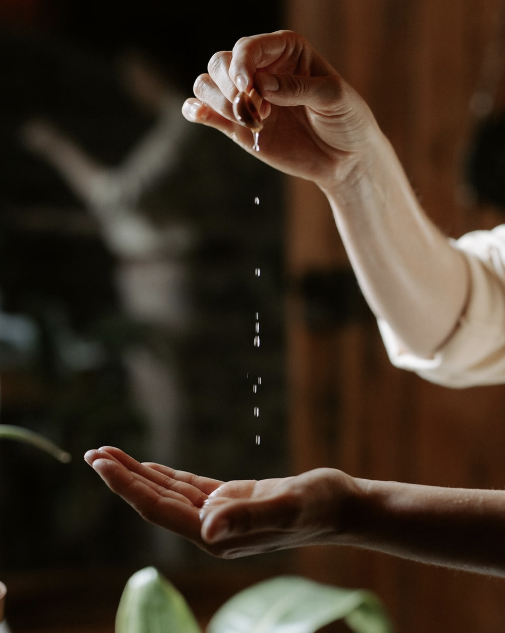 Une main verse une goutte de liquide sur une autre main dans un intérieur chaleureux.