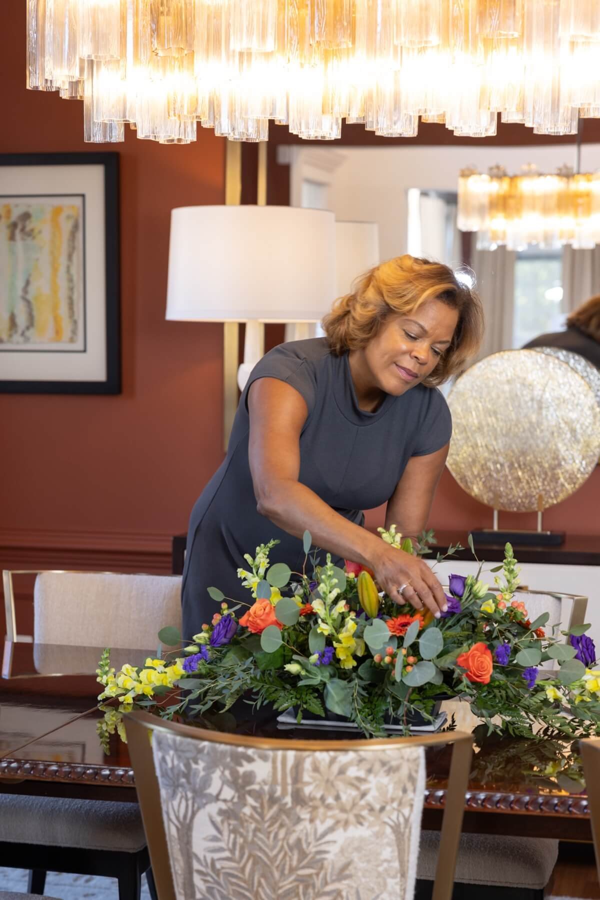 Monique arranging a colorful flower bouquet on a dining table in a well-decorated room.