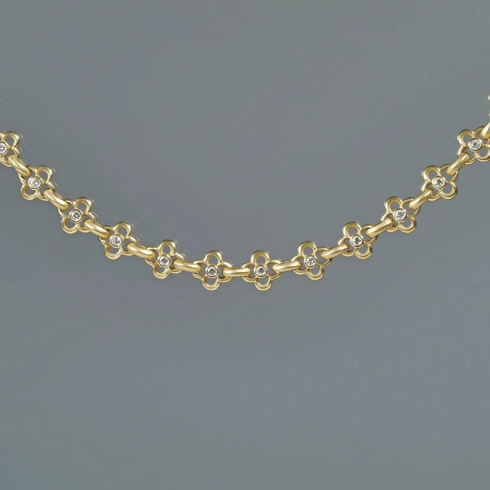 Gold necklace with small flower-shaped links, each decorated with a small diamond in the center, displayed against a gray background, auctioned and photographed by ACES Gallery.