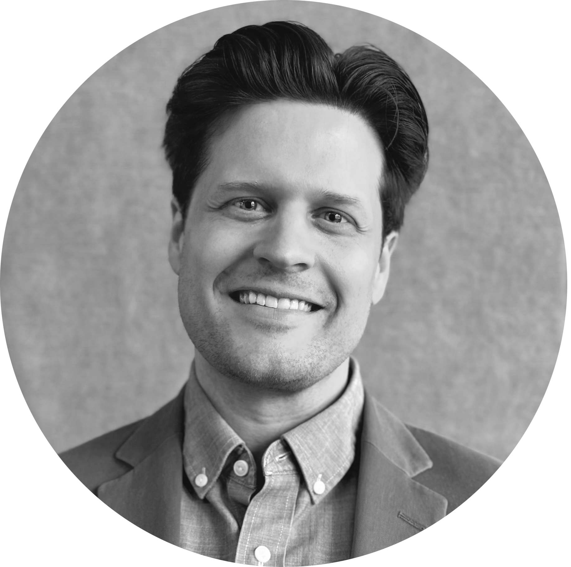 Headshot of a smiling man with dark, styled hair, wearing a light blue button-up shirt and a green blazer against a neutral background.