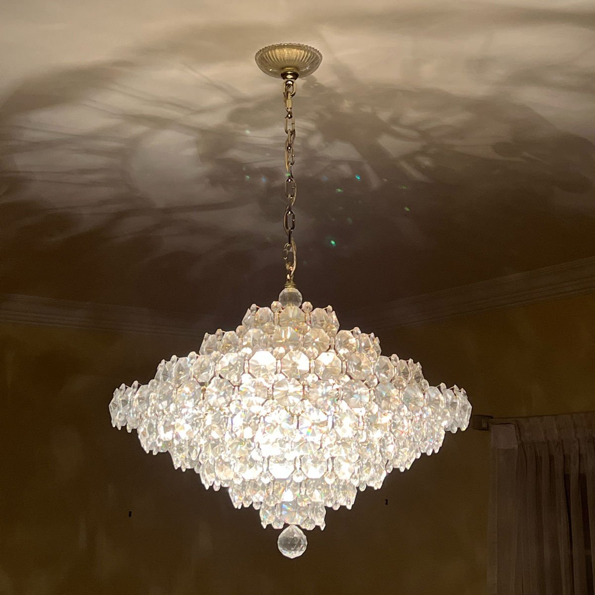 A luxurious crystal chandelier hanging from a ceiling, casting intricate reflections and shadows on the ceiling.