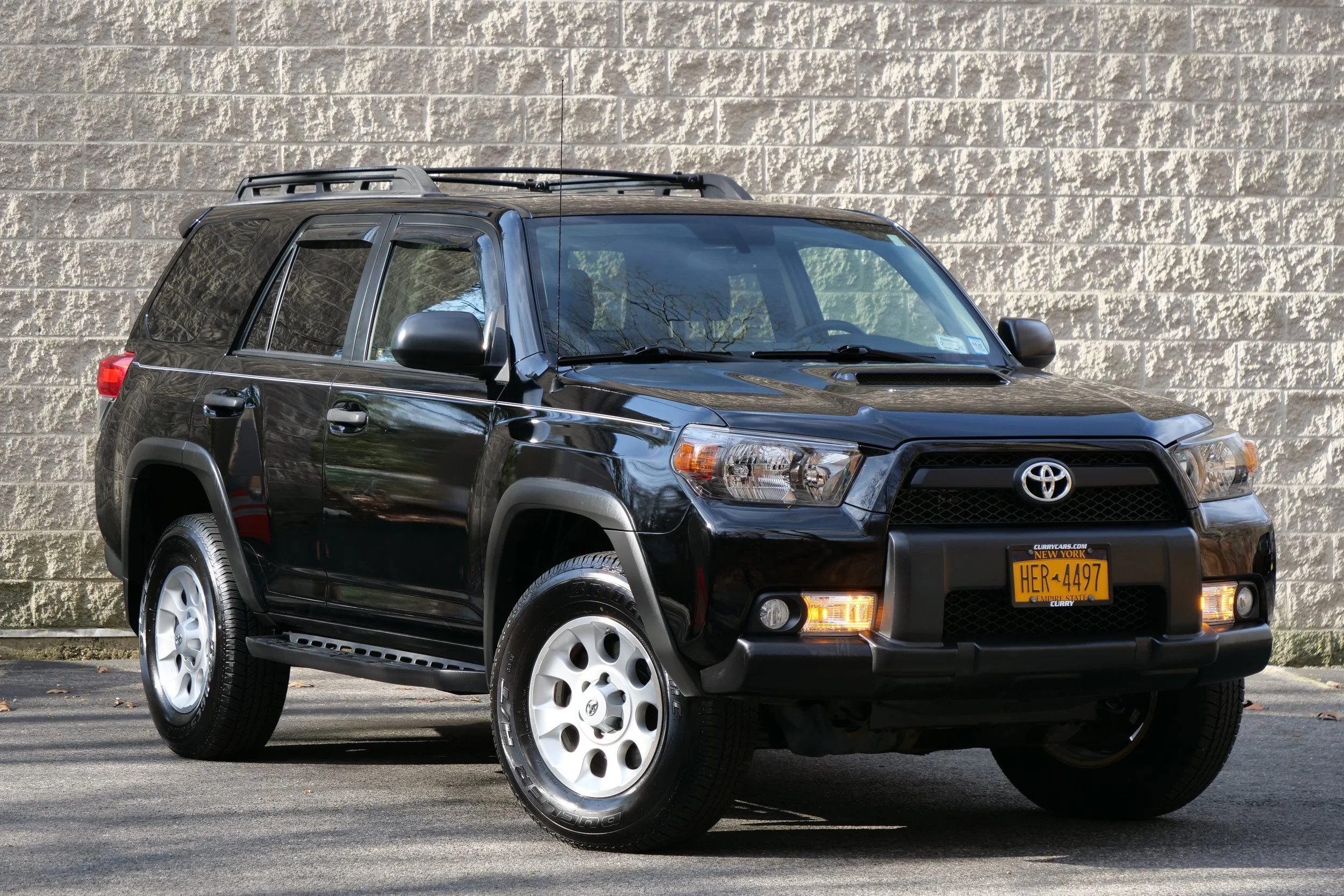 Black Toyota SUV parked in front of a beige brick wall