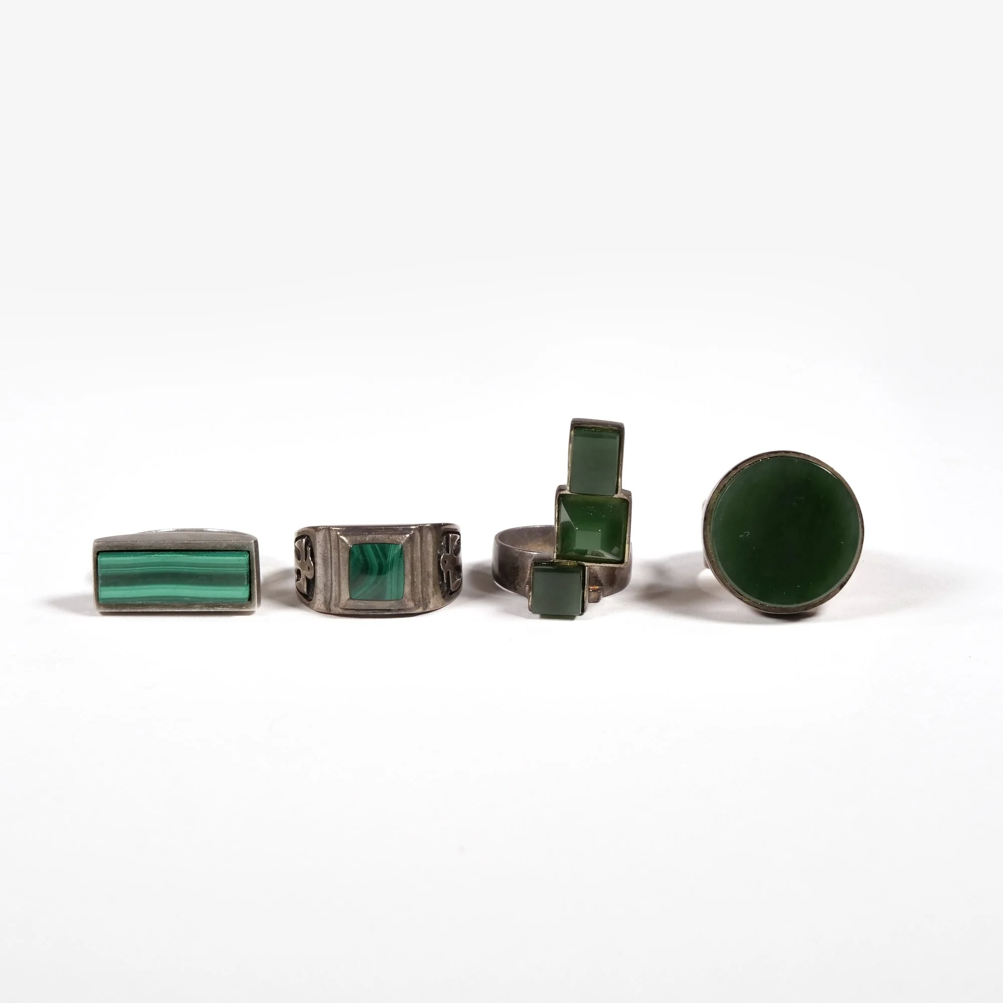 Four silver rings with green stones or inlays, displayed in a row against a white background, auctioned and photographed by ACES Gallery.
