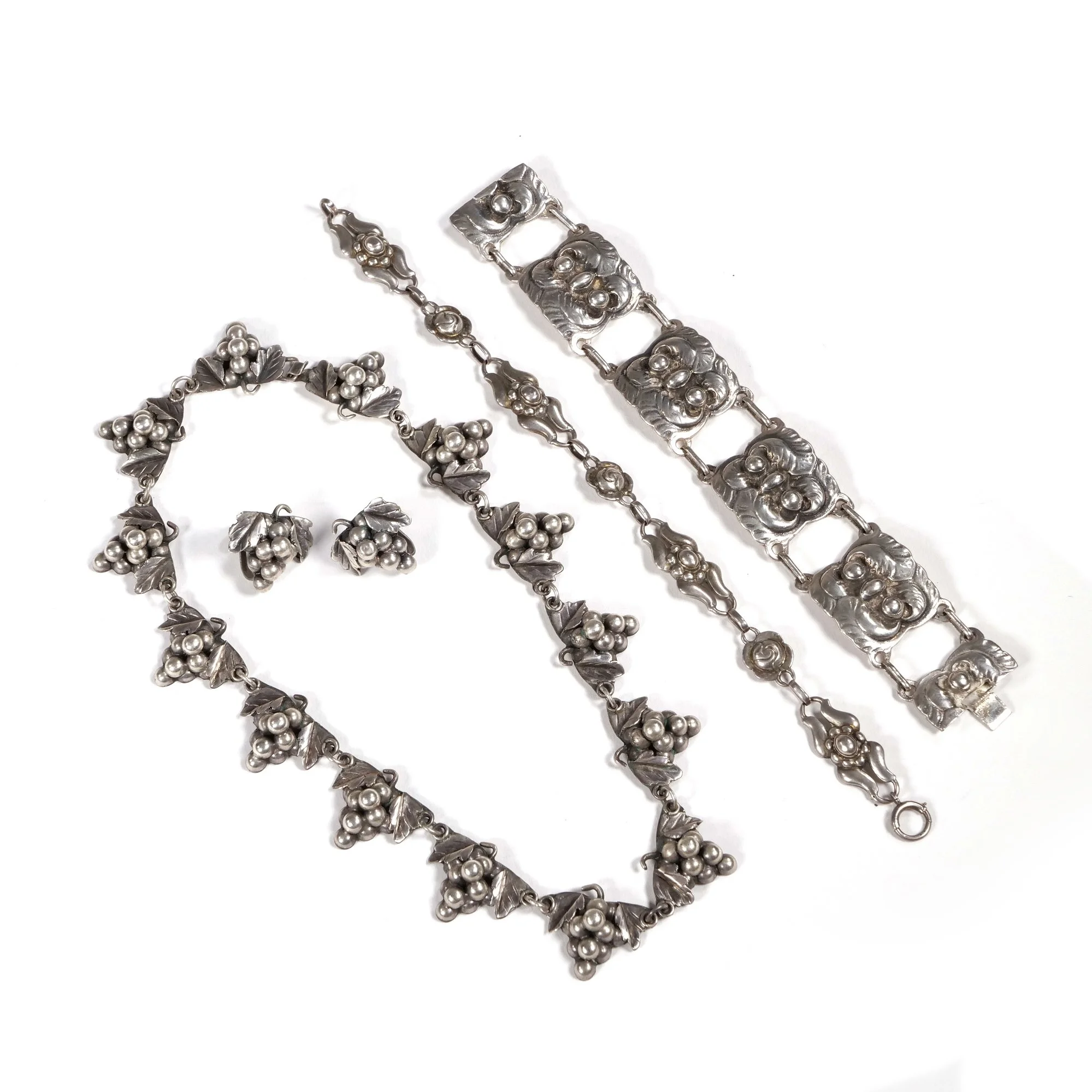 Silver jewelry set with floral designs and pearl accents, including a necklace, bracelet, ring, and chain, auctioned and photographed by ACES Gallery.