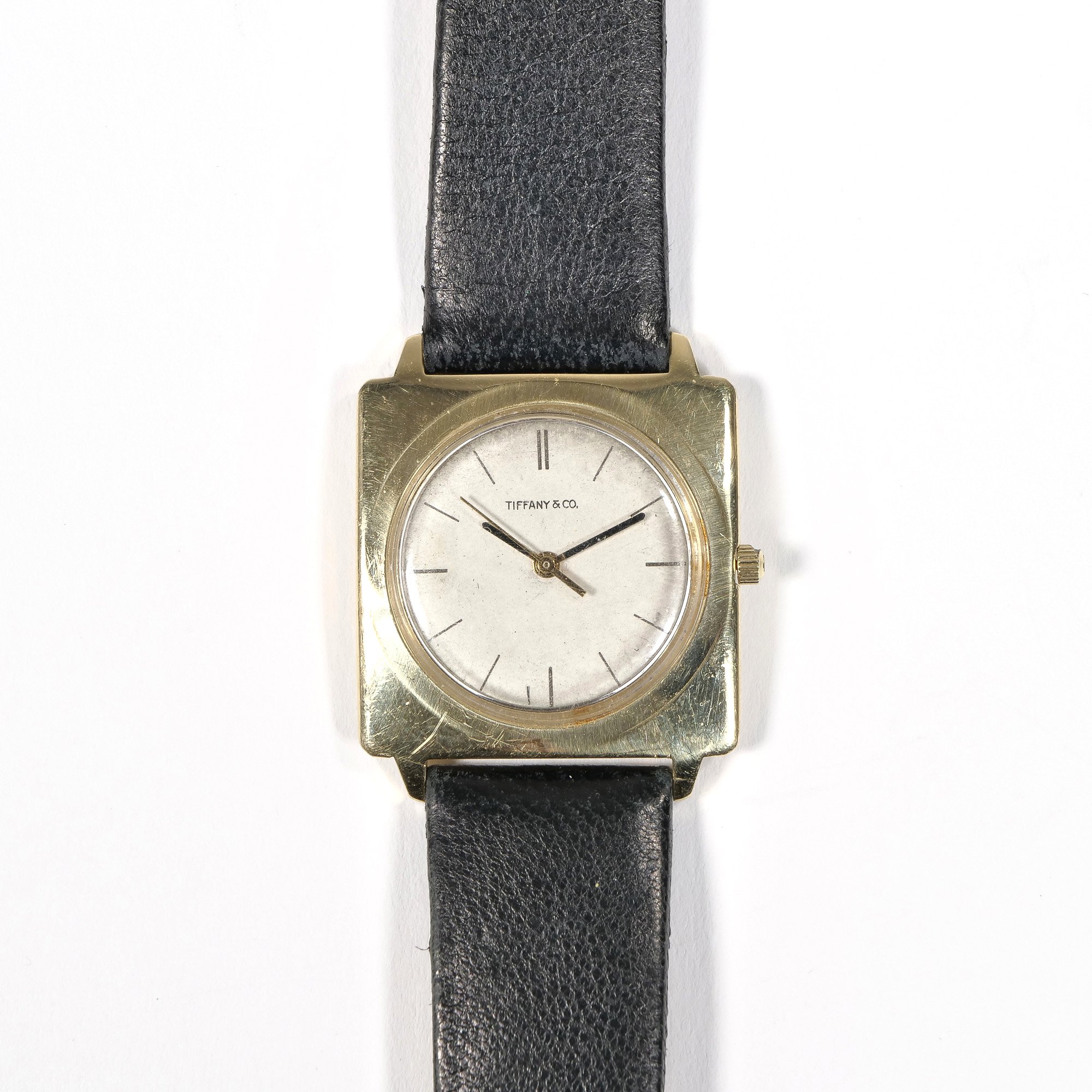 Vintage Tiffany & Co. wristwatch with a square gold-tone case, white dial, and black leather strap, auctioned and photographed by ACES Gallery.