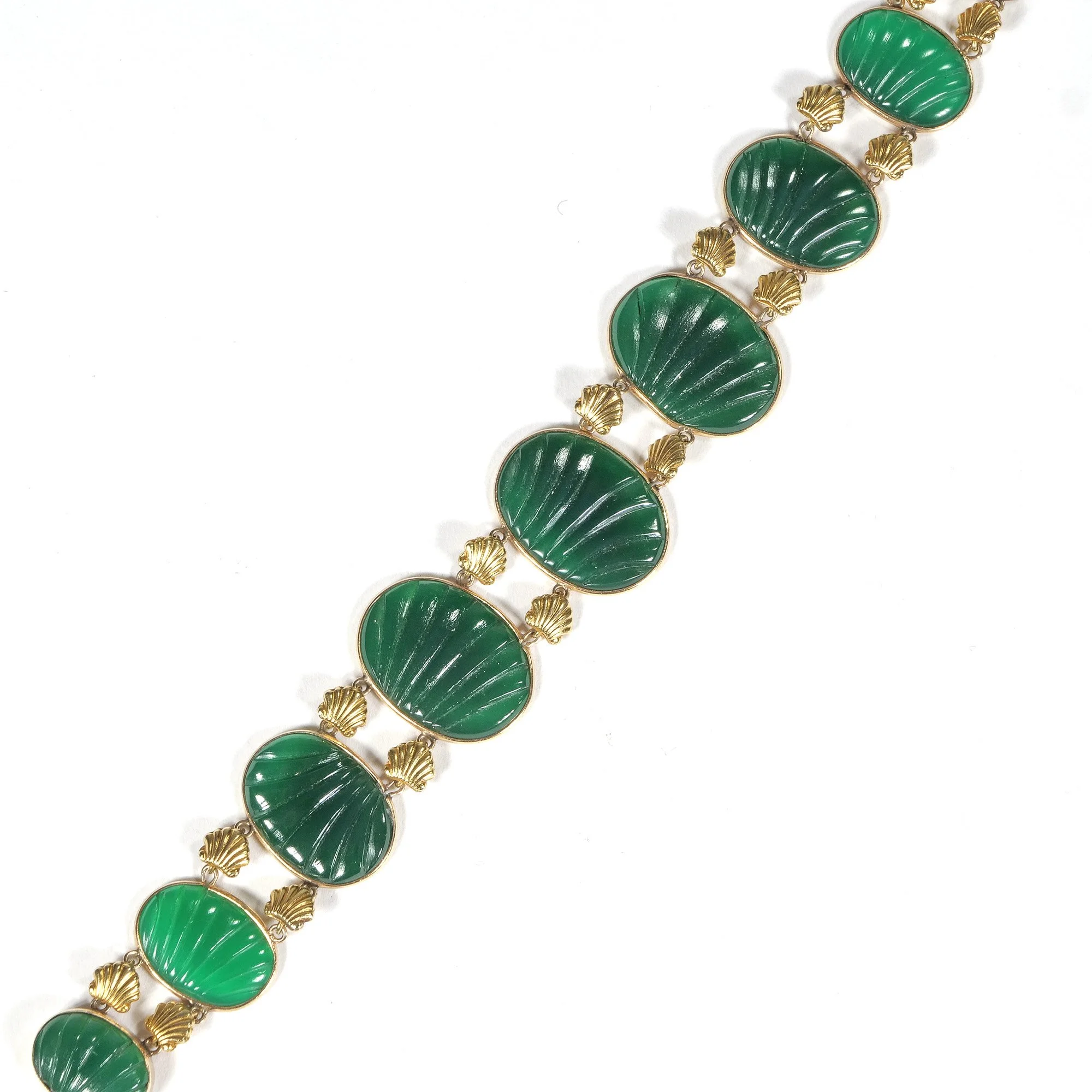 A gold bracelet with large green oval jade carvings and small gold shell-shaped details connecting the stones, arranged in a repeating pattern, auctioned and photographed by ACES Gallery.