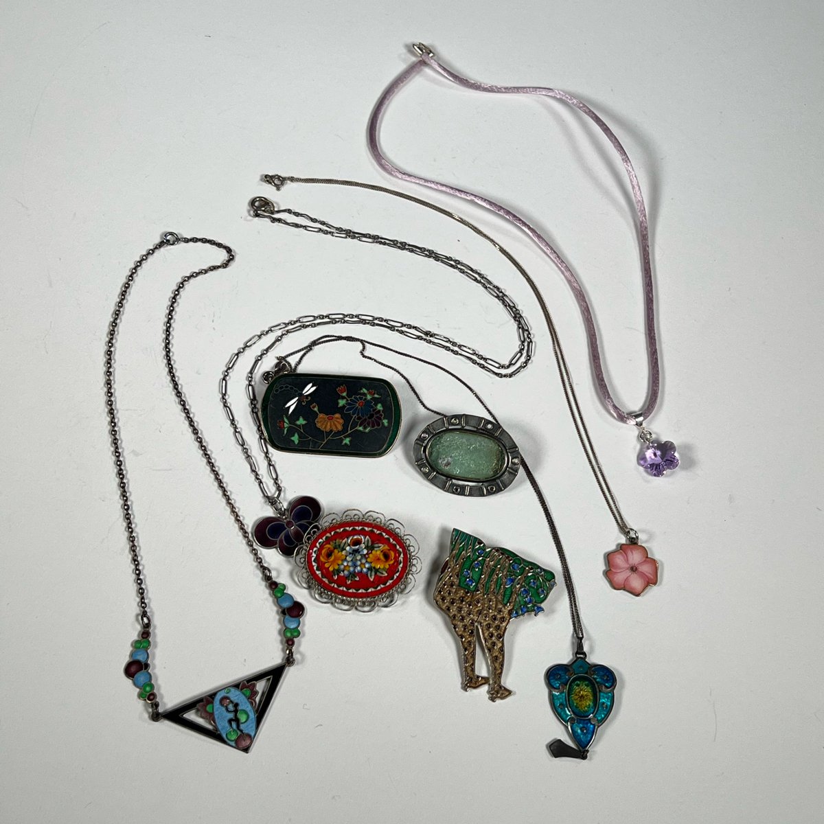 Collection of various necklaces and brooches on a white surface, including floral and colorful designs, auctioned and photographed by ACES Gallery.