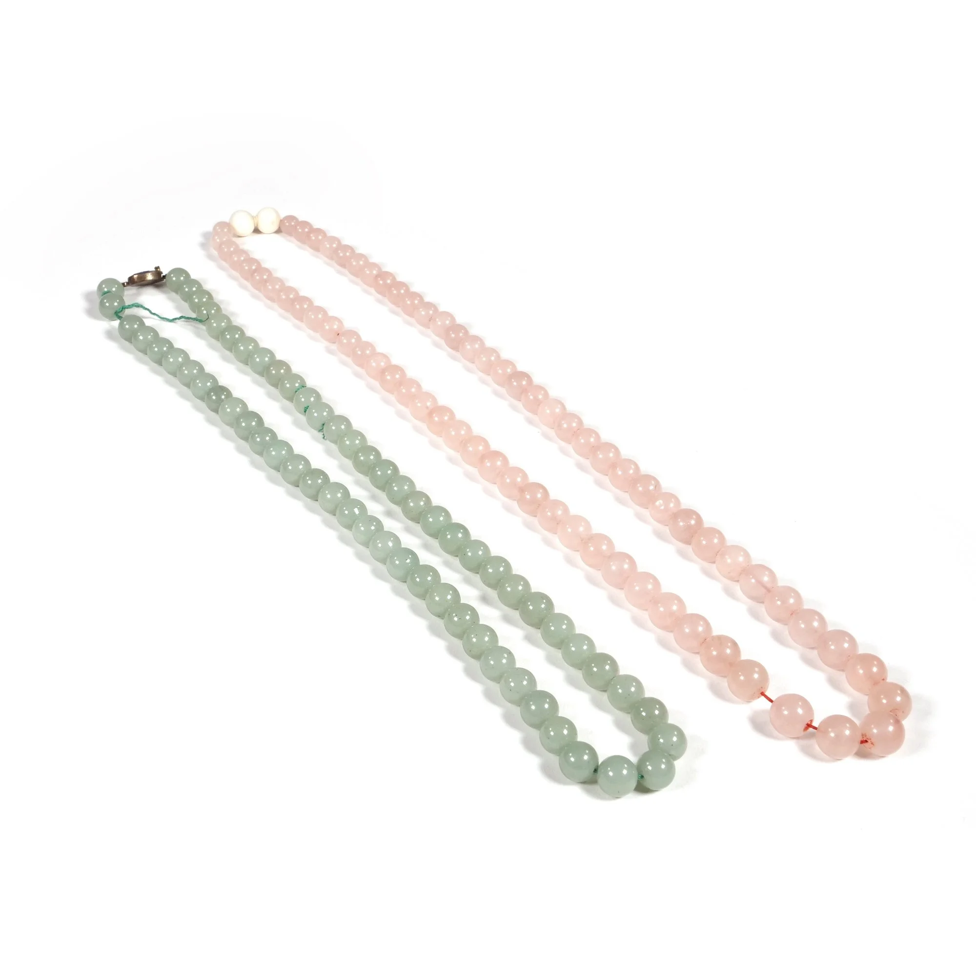 Two pearl necklaces, one pink and one light green, lying on a white background, auctioned and photographed by ACES Gallery.