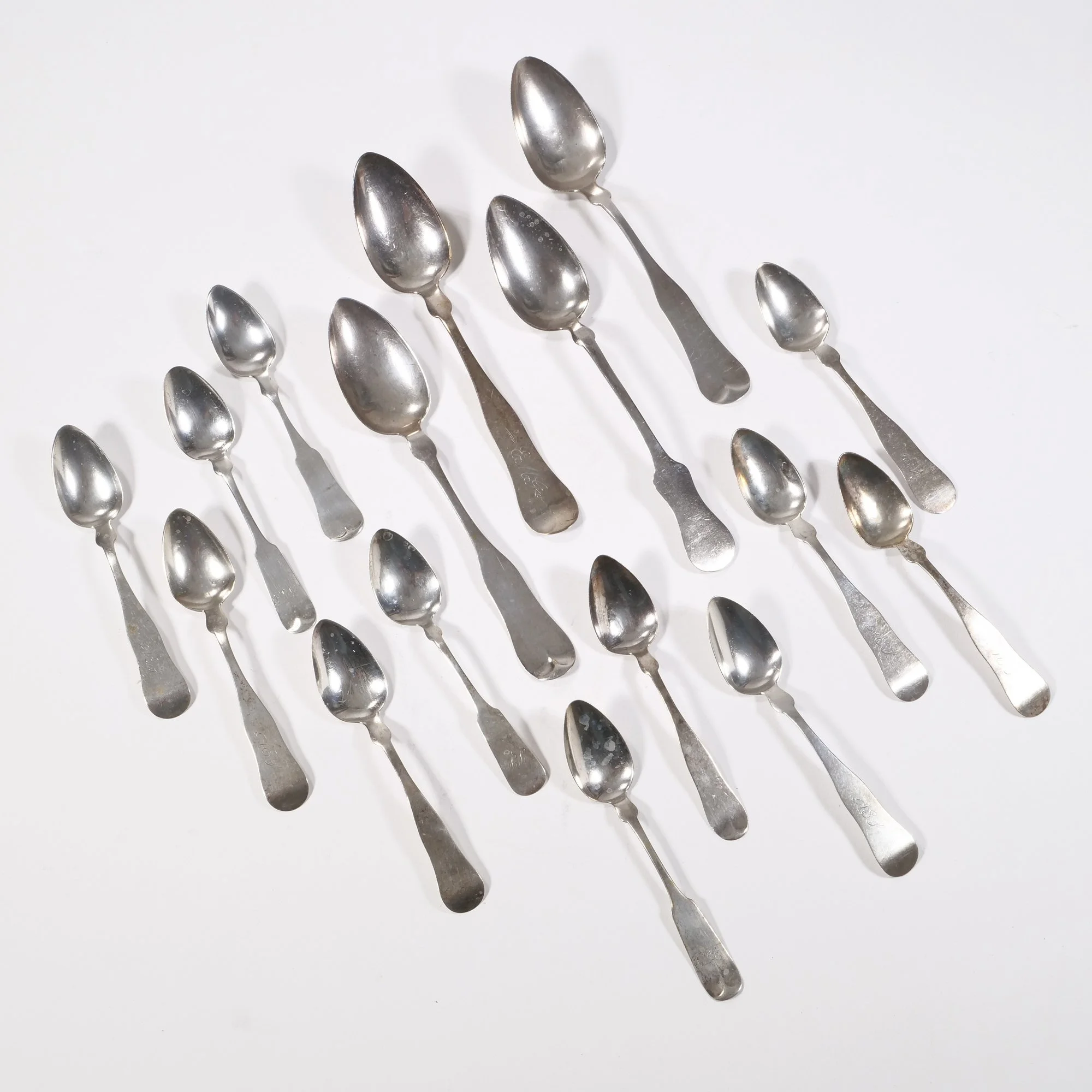 Collection of various sizes silver spoons on a white surface, auctioned and photographed by ACES Gallery.