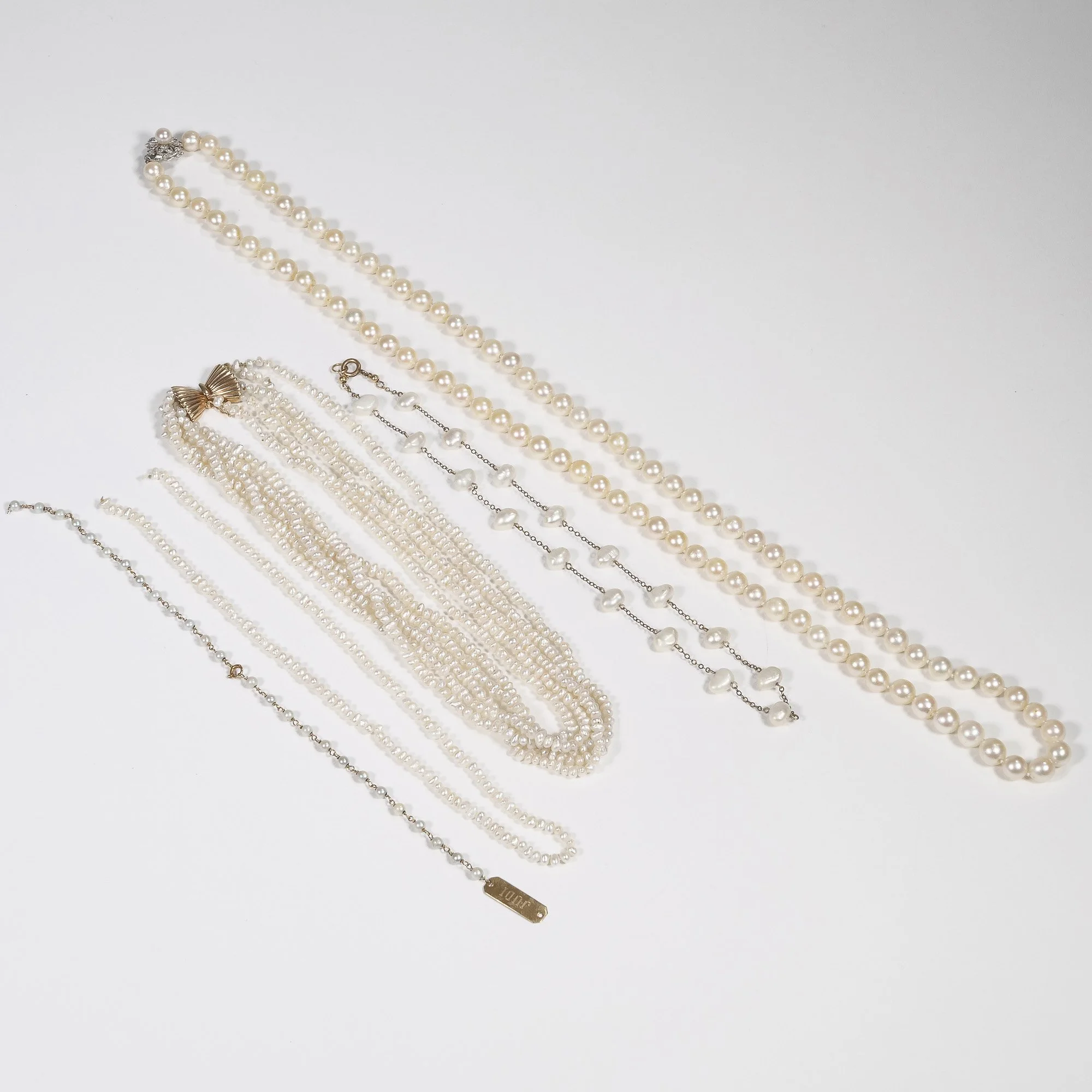 Collection of pearl necklaces and bracelets on a white surface, auctioned and photographed by ACES Gallery.