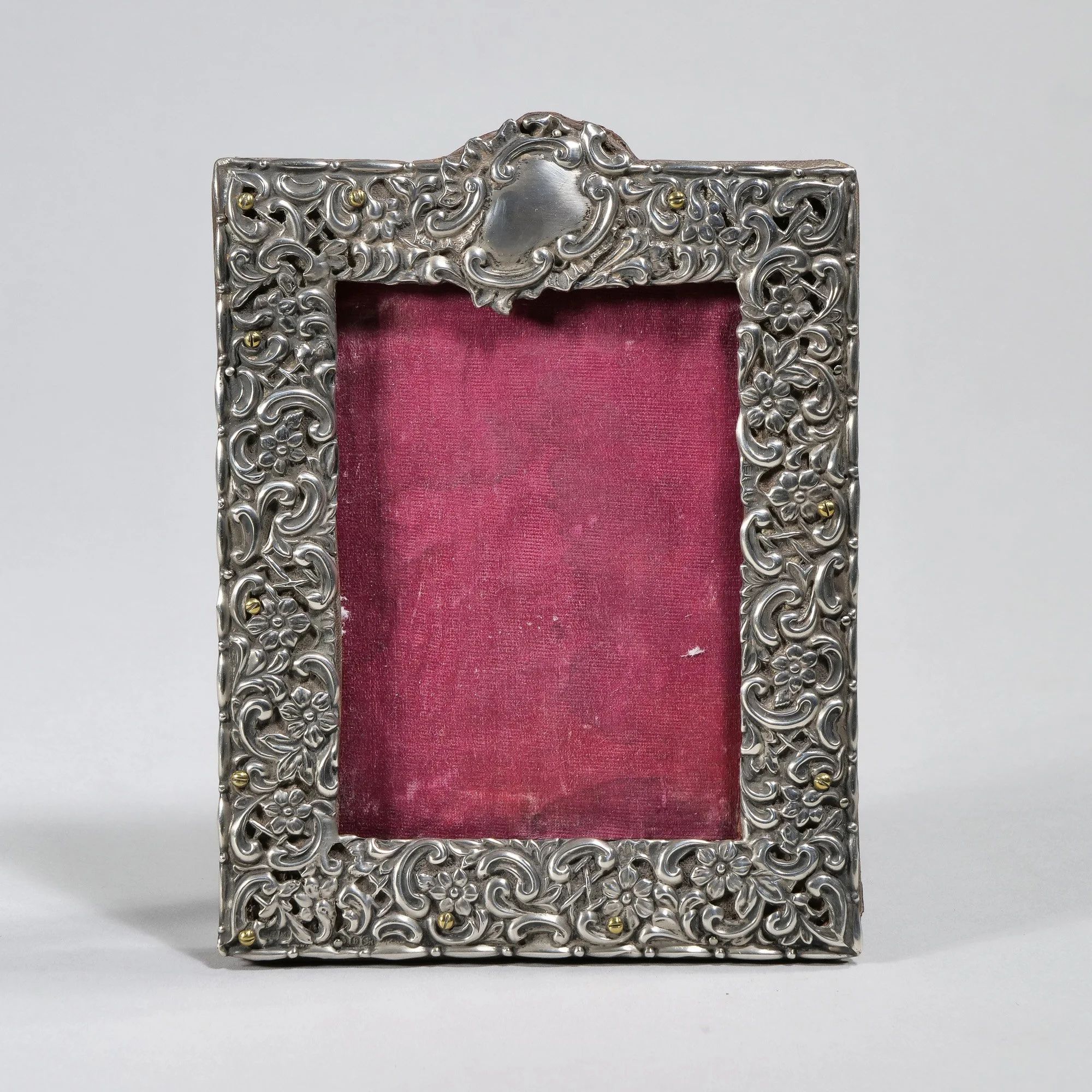 Decorative silver picture frame with floral engravings, empty with pink fabric backing, auctioned and photographed by ACES Gallery.