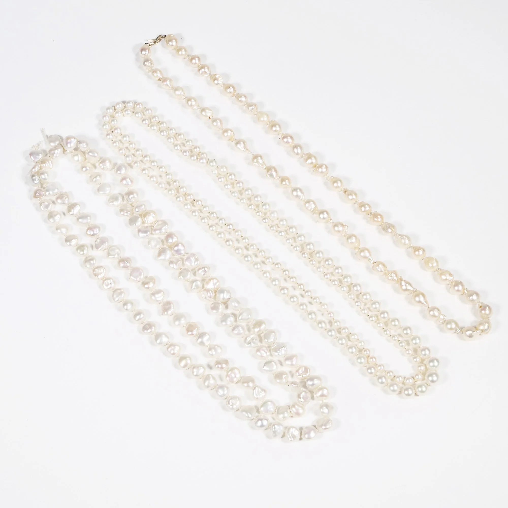 Three pearl necklaces on a white background, auctioned and photographed by ACES Gallery.