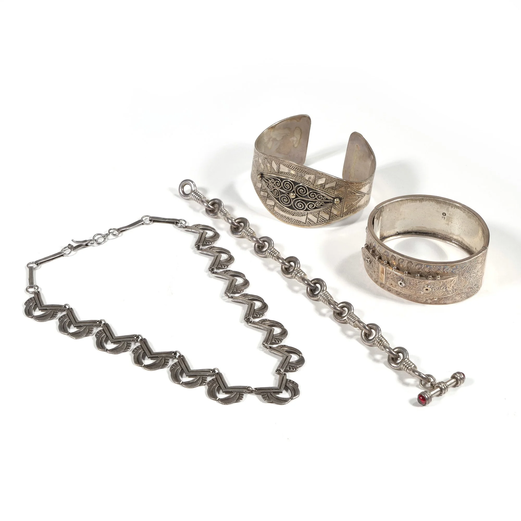 Set of three silver jewelry pieces including a bracelet, a narrow cuff bracelet, and a wide engraved cuff bracelet, displayed on a white surface, auctioned and photographed by ACES Gallery.