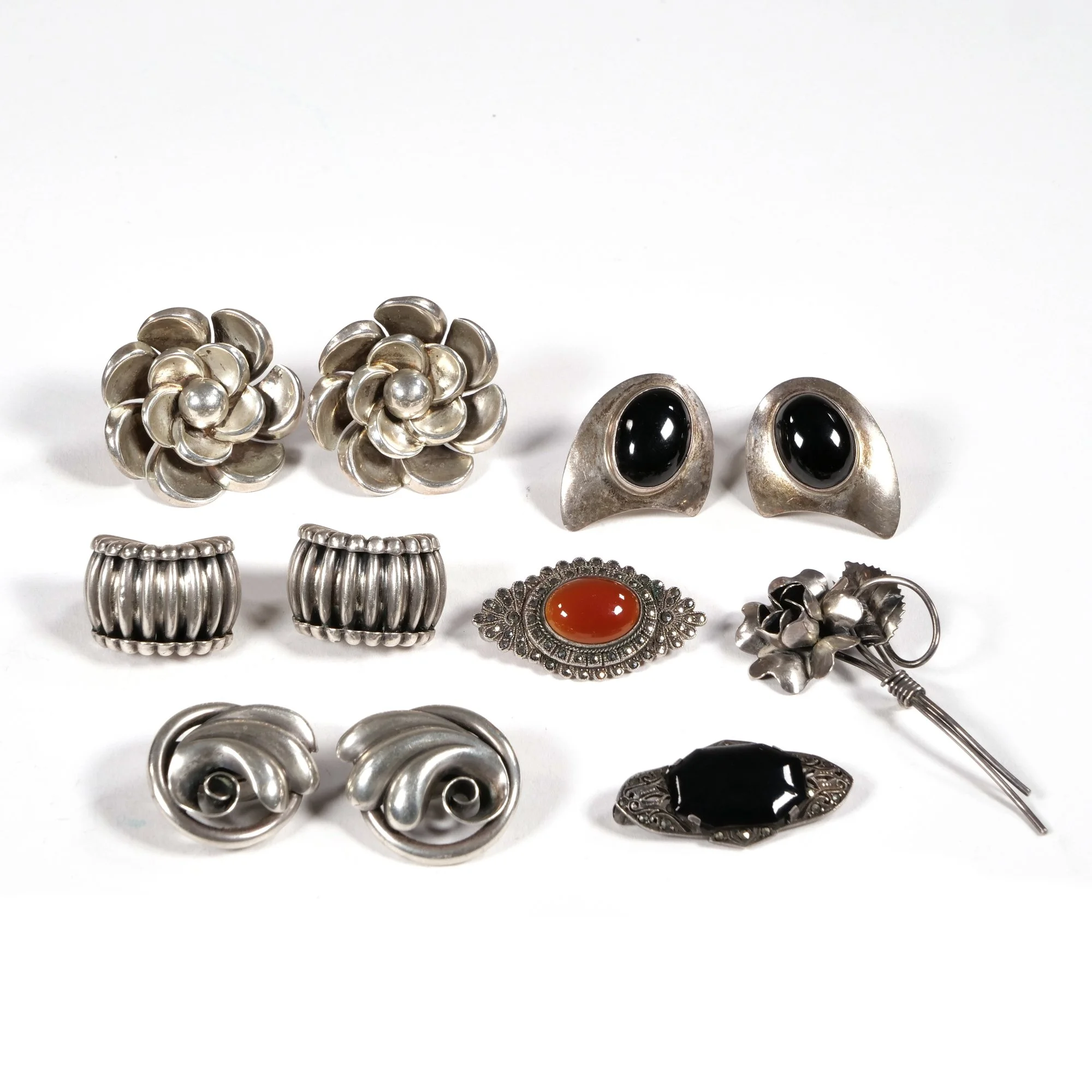 Collection of vintage silver jewelry including earrings, rings, a brooch, and a pin, with black, red, and silver stones, auctioned and photographed by ACES Gallery.