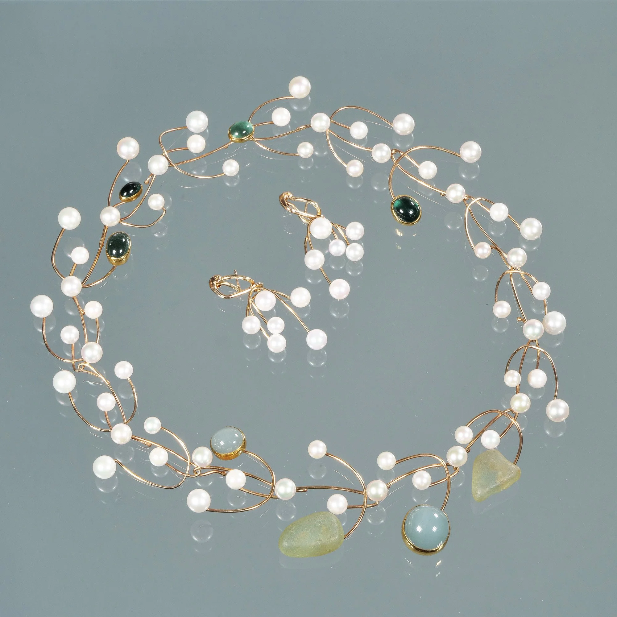 A pearl and gemstone jewelry set consisting of a circular necklace and matching earrings on a reflective gray surface, auctioned and photographed by ACES Gallery.