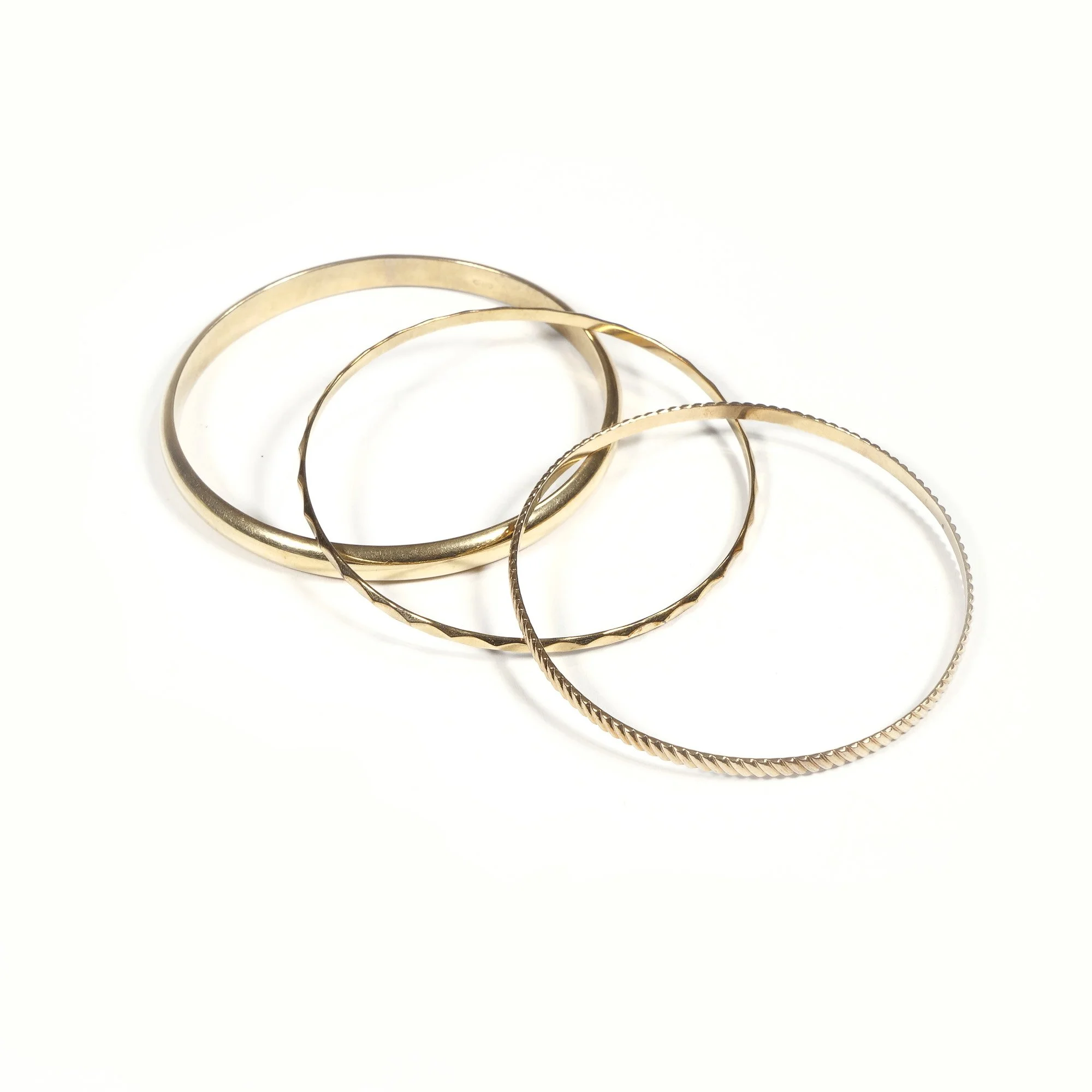 Four gold bangle bracelets with different textures on a white background, auctioned and photographed by ACES Gallery.