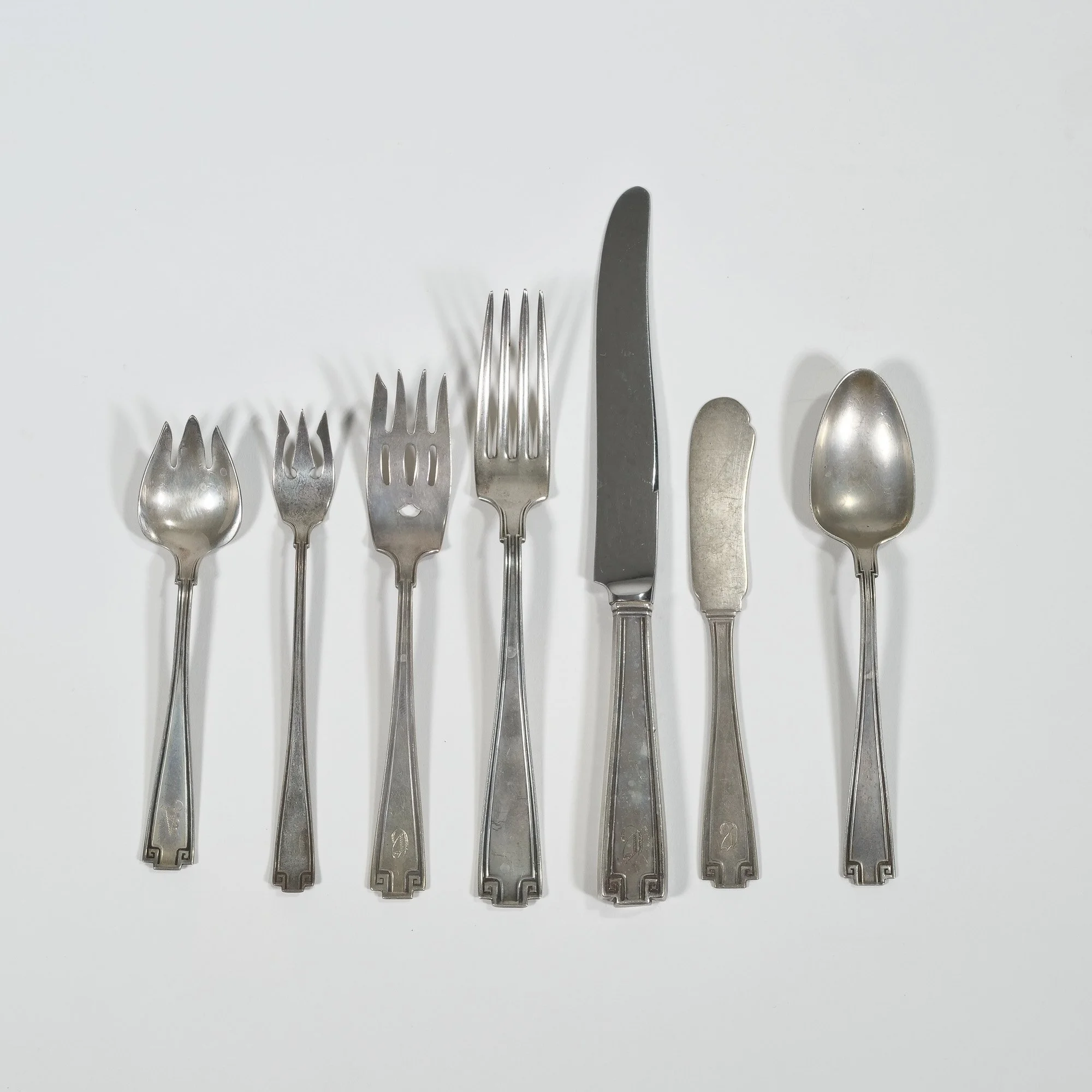 A collection of six sterling silver eating utensils arranged in a row on a white background, including spoons, forks, and knives, auctioned and photographed by ACES Gallery.