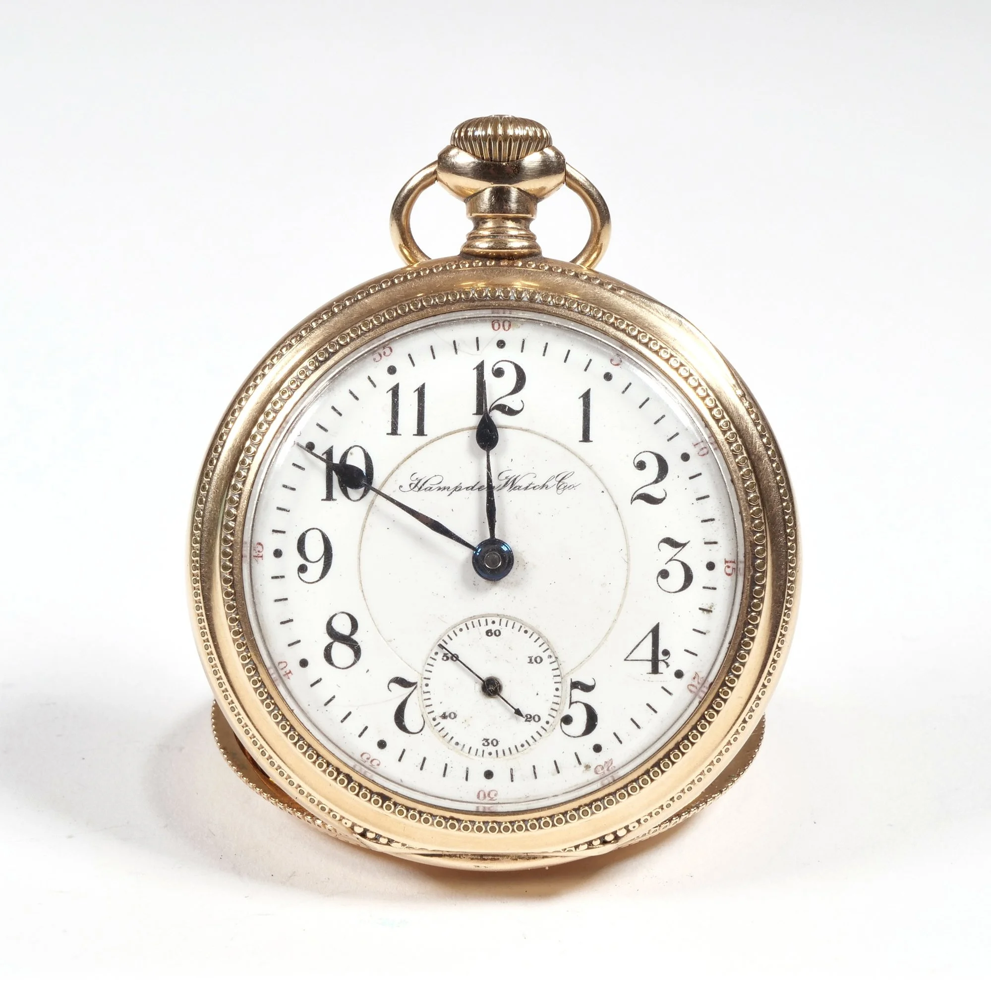 Gold pocket watch with white face, black Arabic numerals, and black hands showing 12:50, on a white background, auctioned and photographed by ACES Gallery.