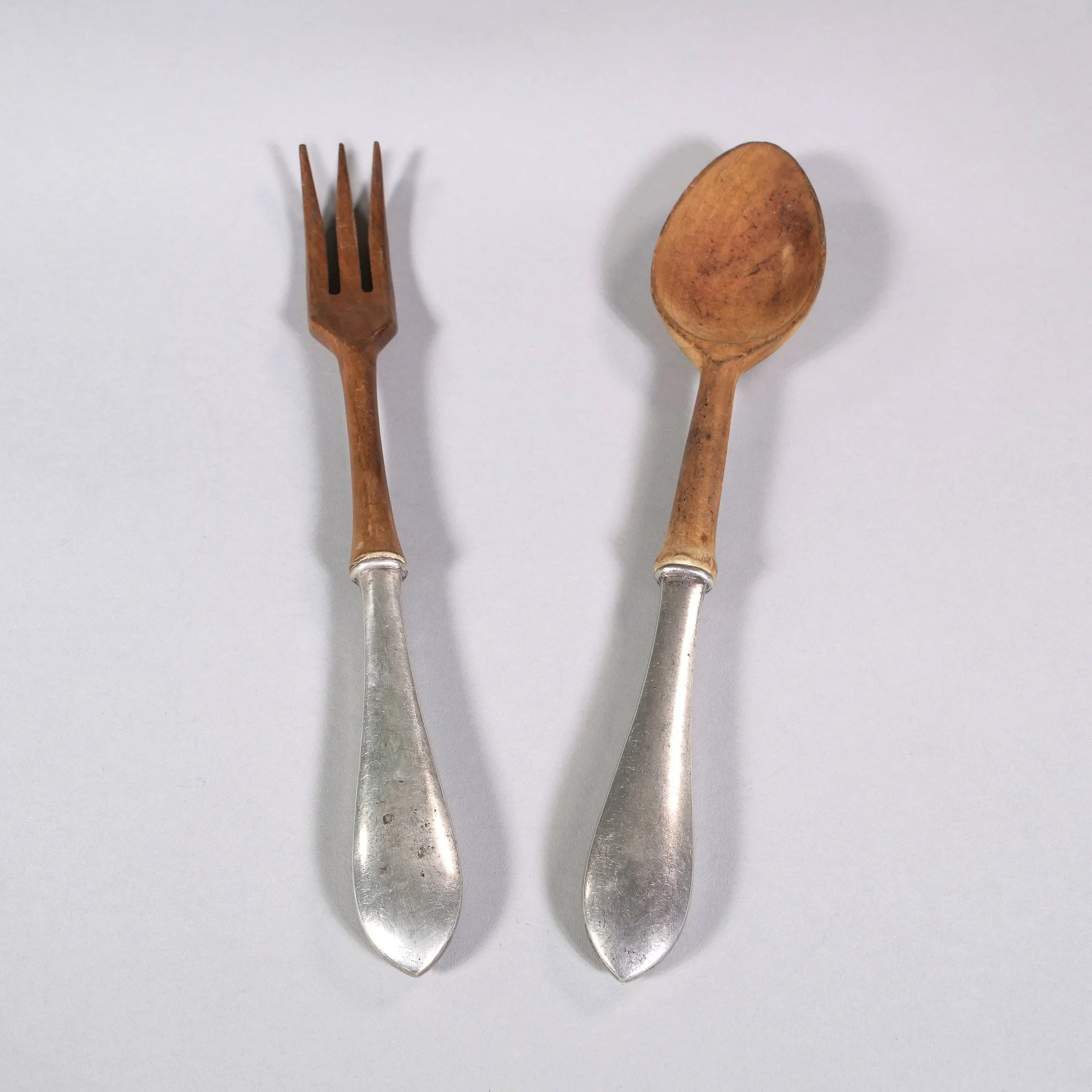 A wooden fork and spoon salad servers with sterling silver handles placed on a white surface, auctioned and photographed by ACES Gallery.