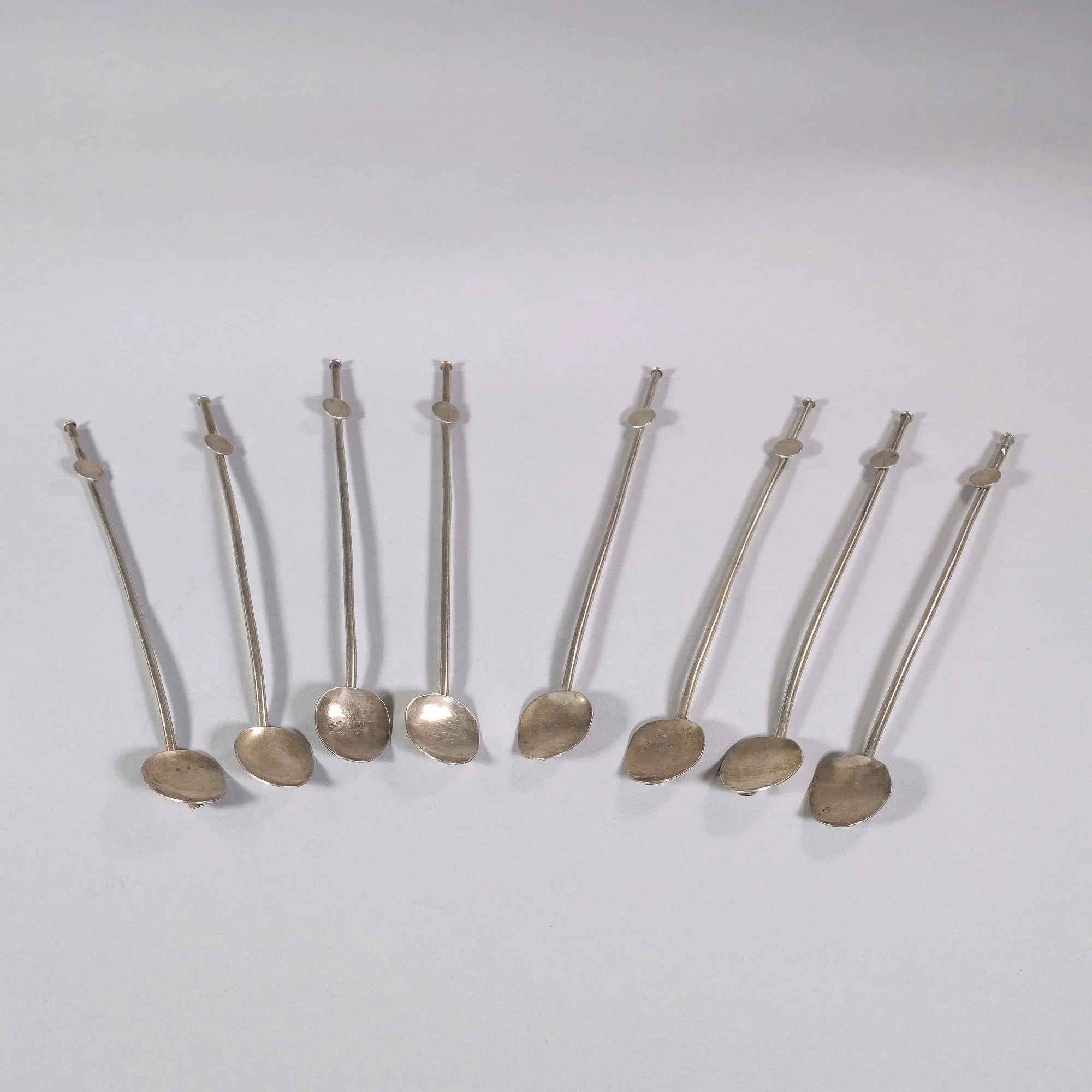 Set of ten silver spoon-shaped pins with flat round heads, arranged in a slight curve on a white background, auctioned and photographed by ACES Gallery.