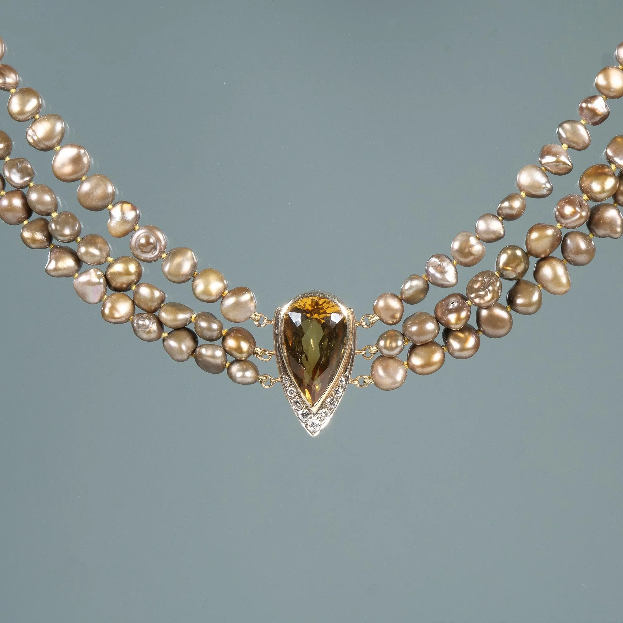 Crossed strands of white and grey pearls with a central pendant featuring a large teardrop-shaped golden-brown gemstone surrounded by small clear stones, auctioned and photographed by ACES Gallery.