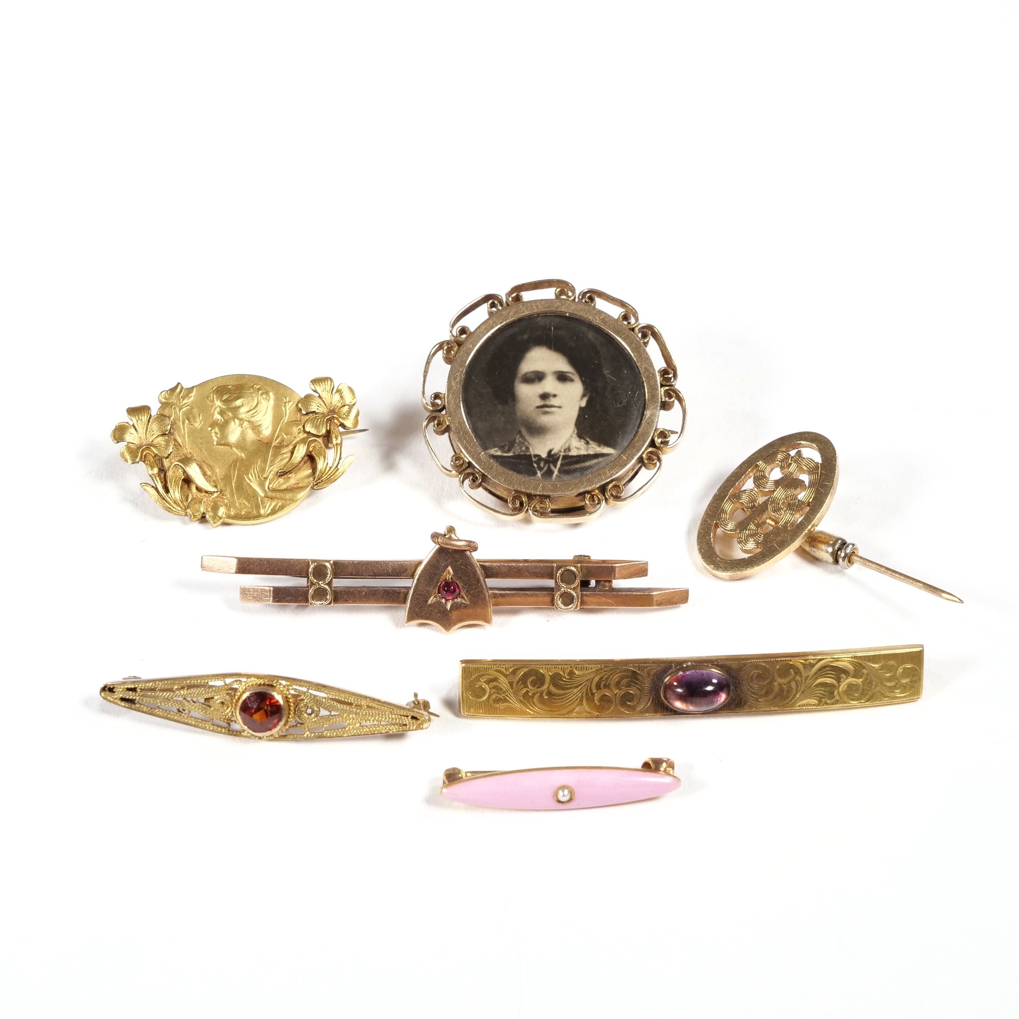 Collection of vintage jewelry including brooches, pendants, and pins with ornate designs and gemstones, along with a black-and-white photograph of a woman in a decorative frame, auctioned and photographed by ACES Gallery.