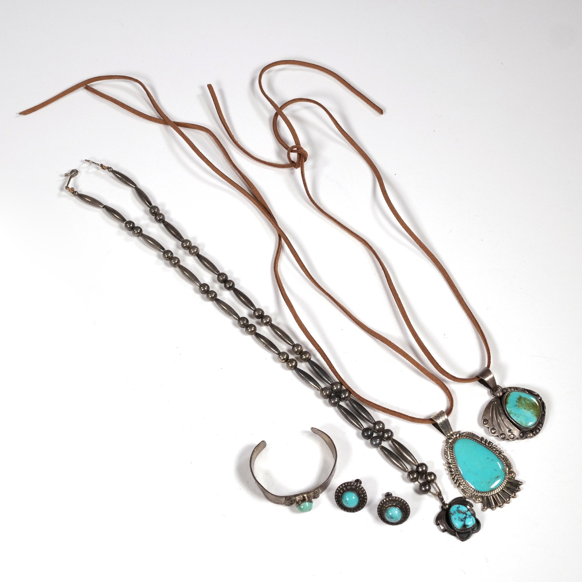 Silver and turquoise jewelry set including two necklaces, earrings, a bracelet, and a ring, displayed on a white background, auctioned and photographed by ACES Gallery.
