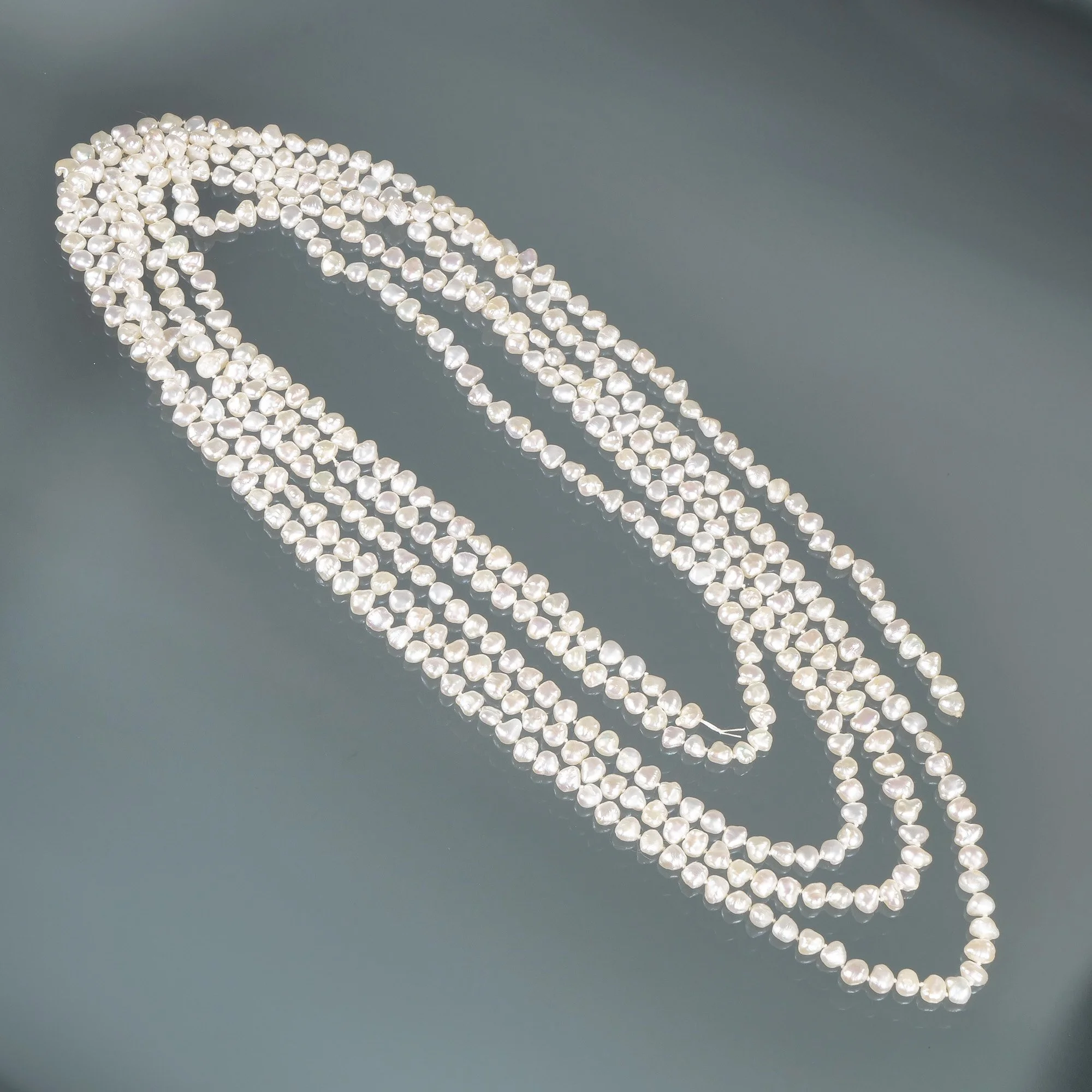 Multiple strands of white pearl necklaces laid out on a gray surface, auctioned and photographed by ACES Gallery.