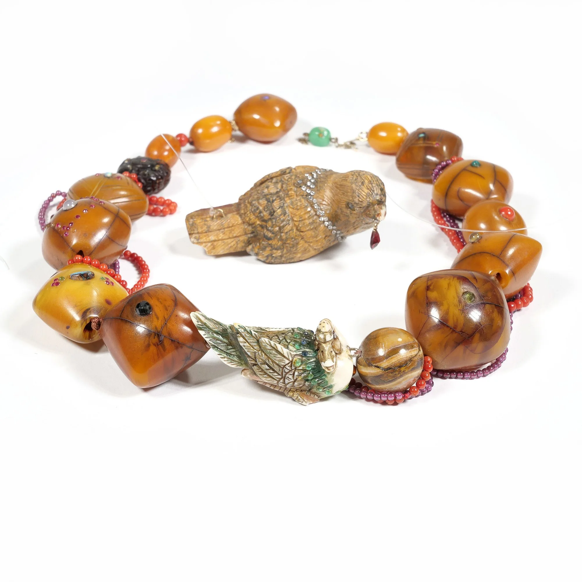 A necklace with large amber beads, a carved wood bird pendant, and a carved shell bird pendant, displayed on a white background, auctioned and photographed by ACES Gallery.