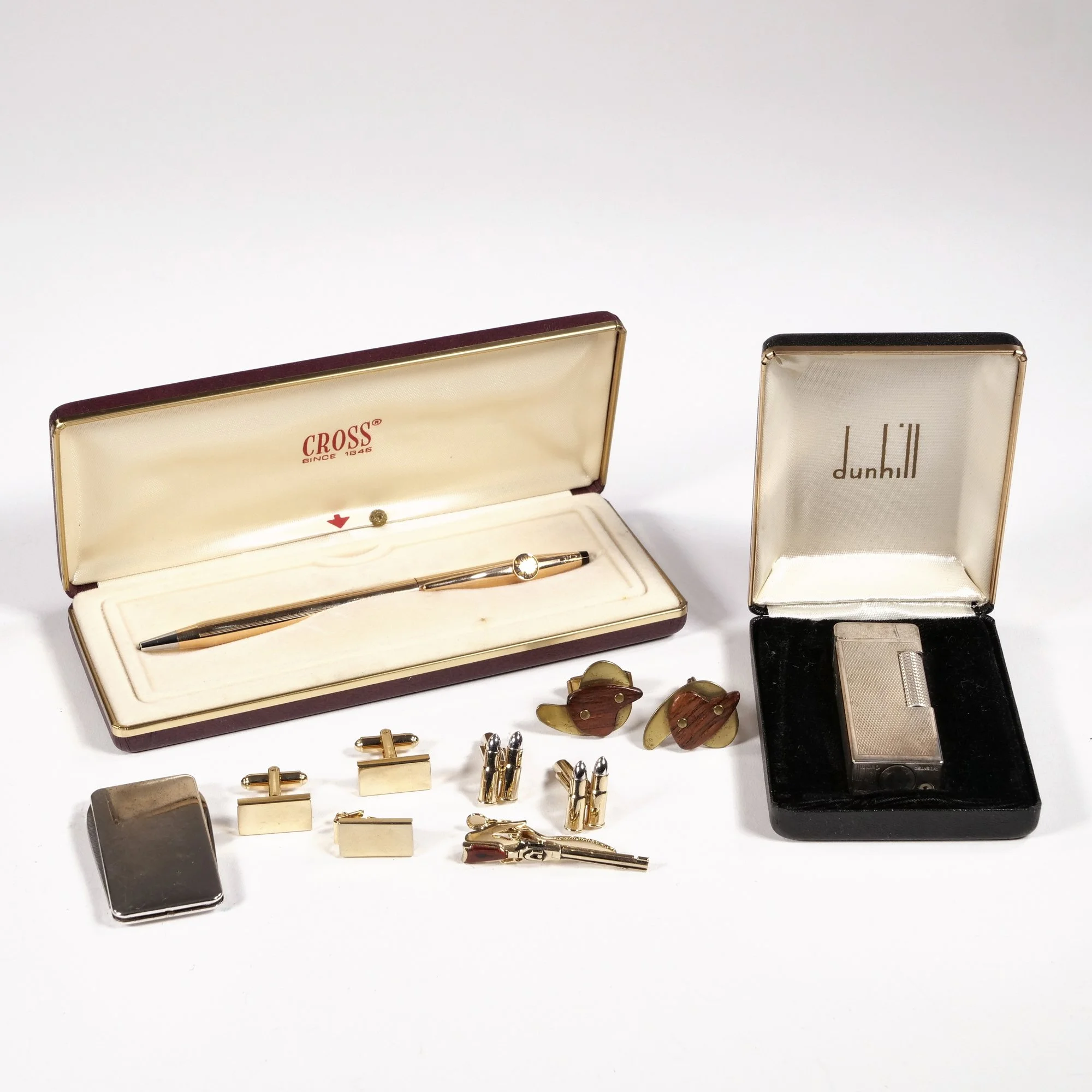 Collection of vintage men's accessories including a gold pen in a jewelry box, gold cufflinks and tie clip, wooden cufflinks, a silver tie clip, a gold tie pin, a small lighter, and a cigarette lighter in a black box, photographed by ACES Gallery.