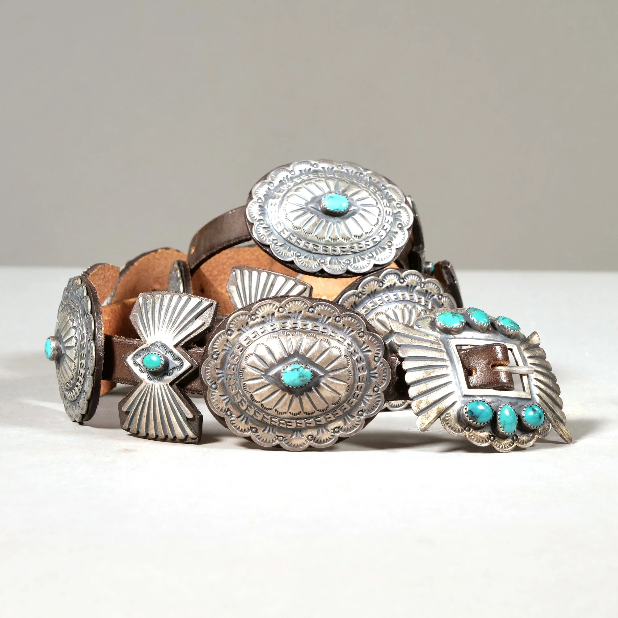 A leather and sterling silver Native American belt with large decorative silver pieces, each featuring intricate patterns and turquoise stones, auctioned and photographed by ACES Gallery.