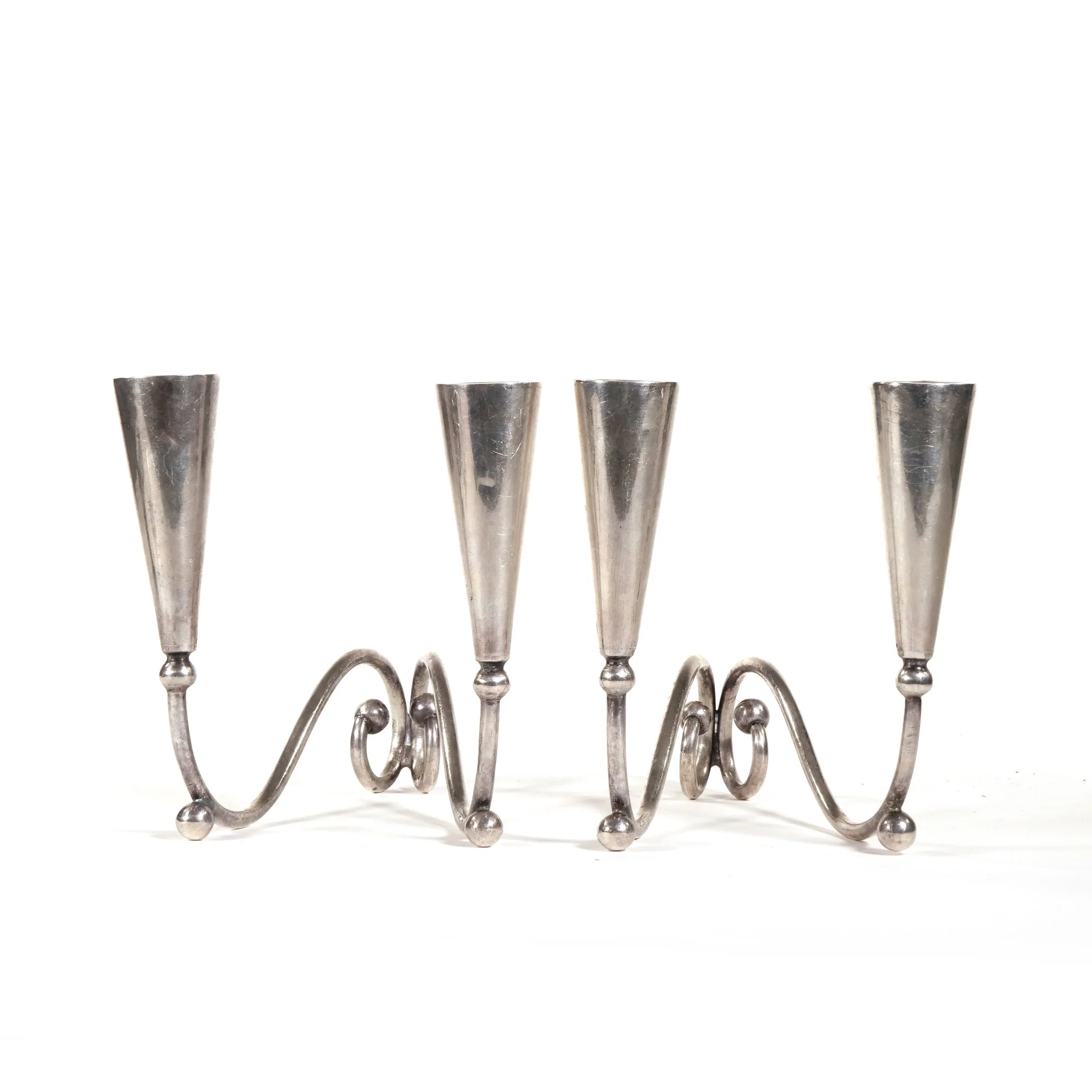A silver metal candle holder with three cone-shaped holders connected by a wavy, decorative base, auctioned and photographed by ACES Gallery.