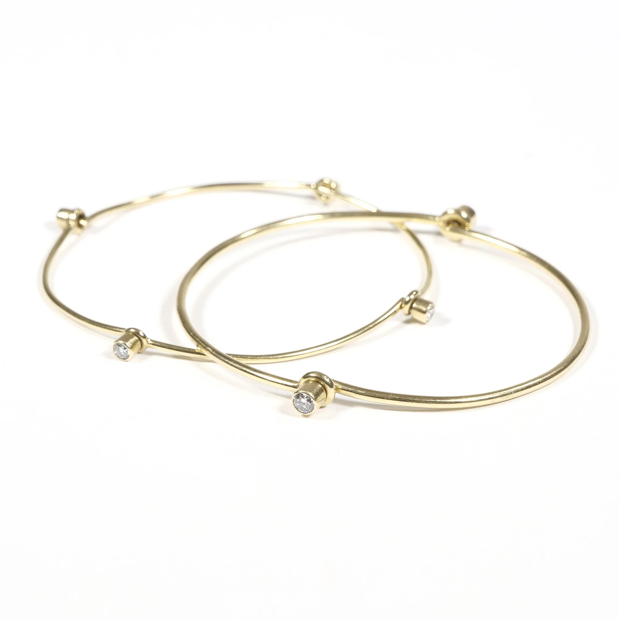Three gold bangle bracelets with small diamonds on a white background, auctioned and photographed by ACES Gallery.