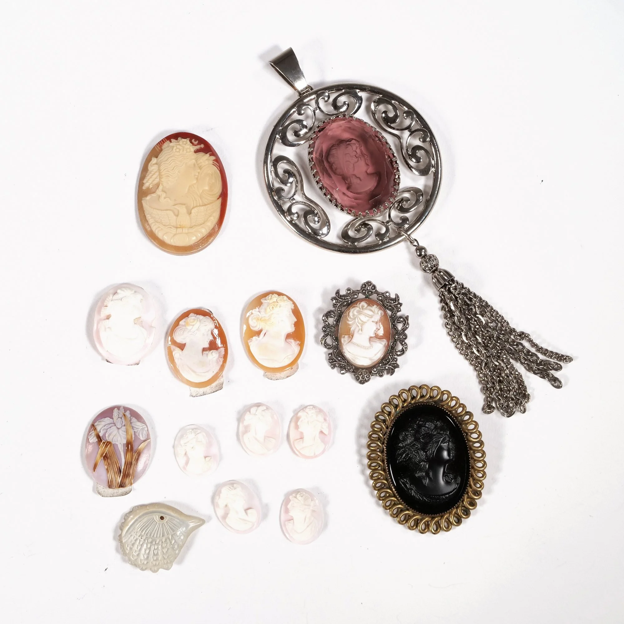 Collection of vintage cameo jewelry including brooches and pendants in various colors and designs displayed on a white surface, auctioned and photographed by ACES Gallery.