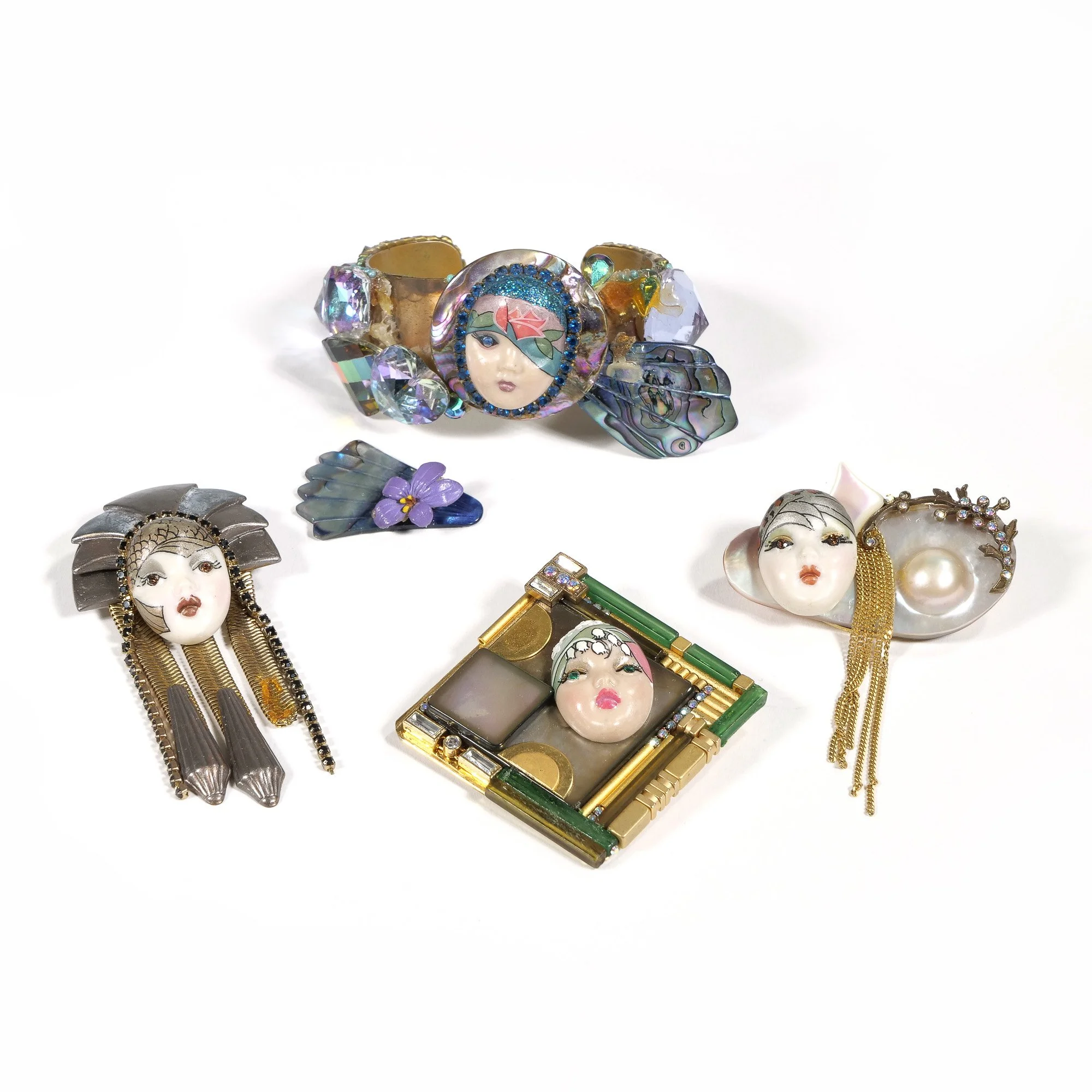 Collection of decorative brooches and pins featuring faces, with various designs and embellishments on a white background, auctioned and photographed by ACES Gallery.