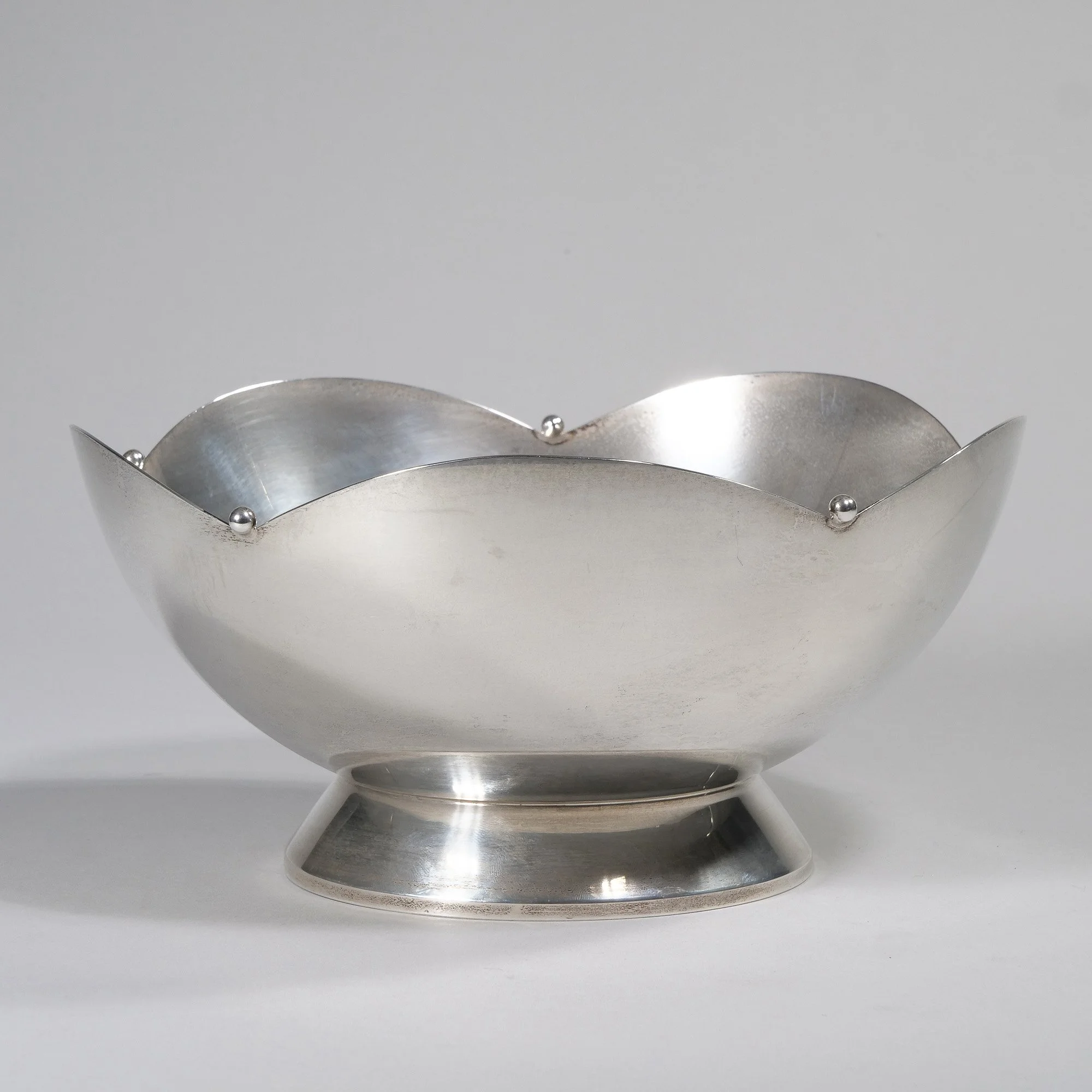 Silver decorative bowl with a scalloped edge and small silver balls at the peaks, placed on a flat surface, auctioned and photographed by ACES Gallery.