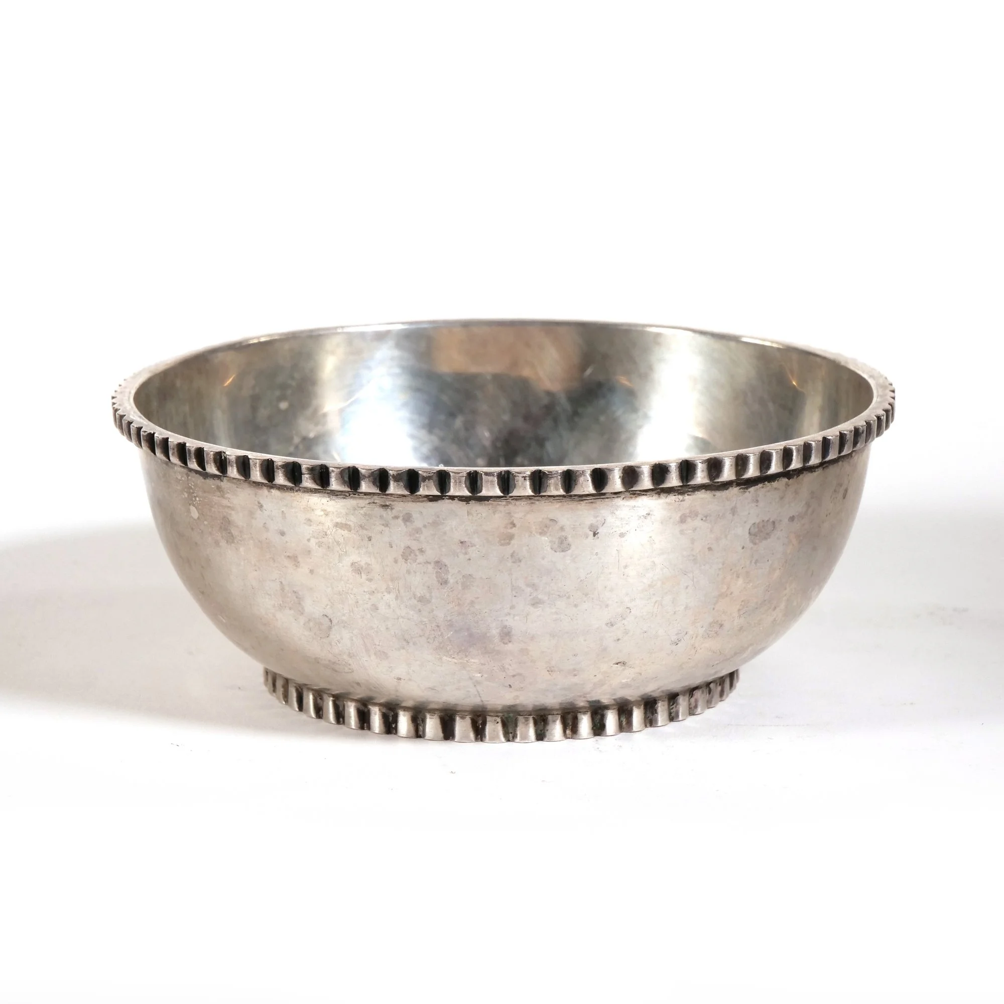 Silver bowl with a beaded edge, showing signs of age and tarnish, placed on a white surface, auctioned and photographed by ACES Gallery.