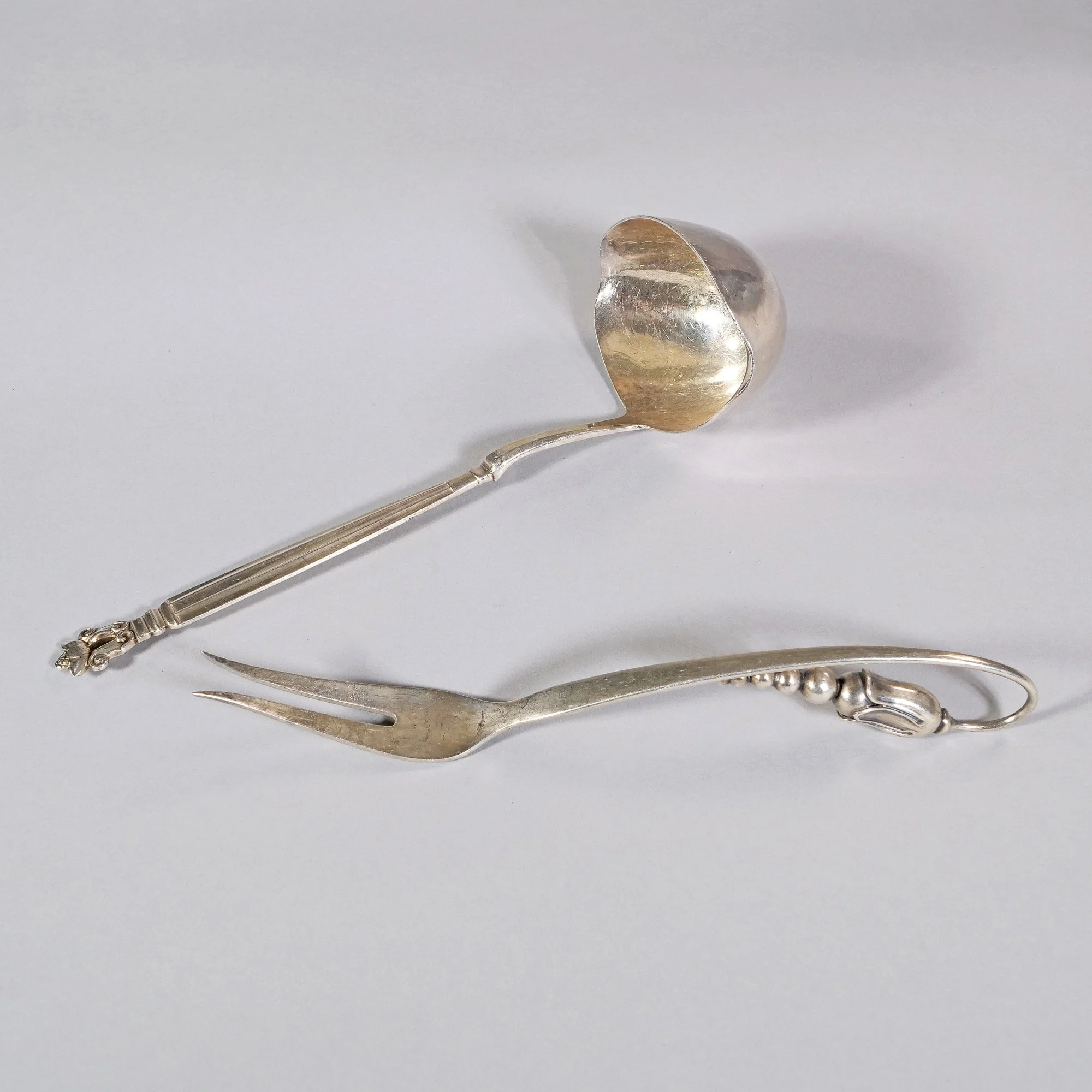 Silver spoon and fork with decorative handles on a white surface, auctioned and photographed by ACES Gallery.