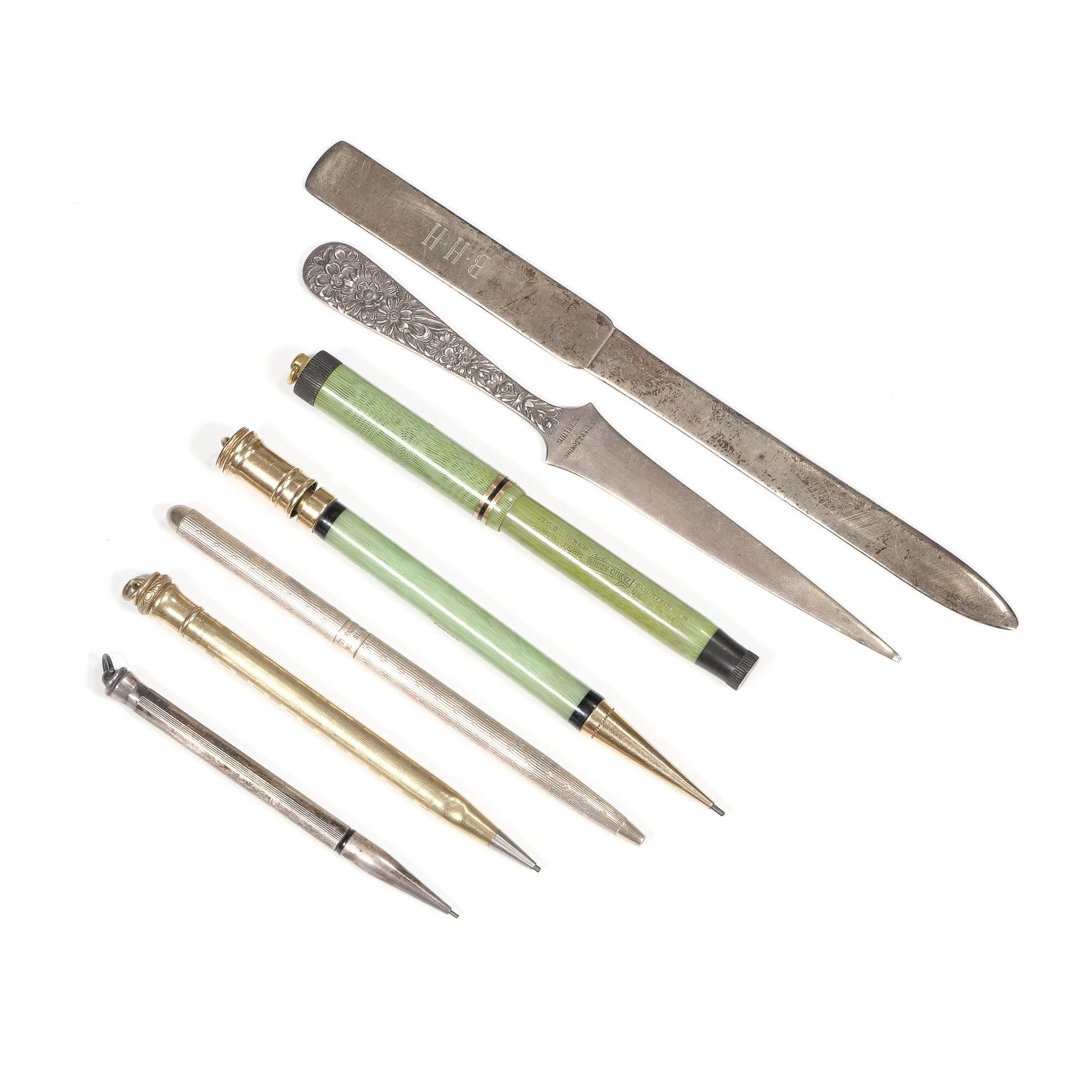 A collection of vintage pens, a letter opener, and a bookbinding knife arranged on a white background, auctioned and photographed by ACES Gallery.