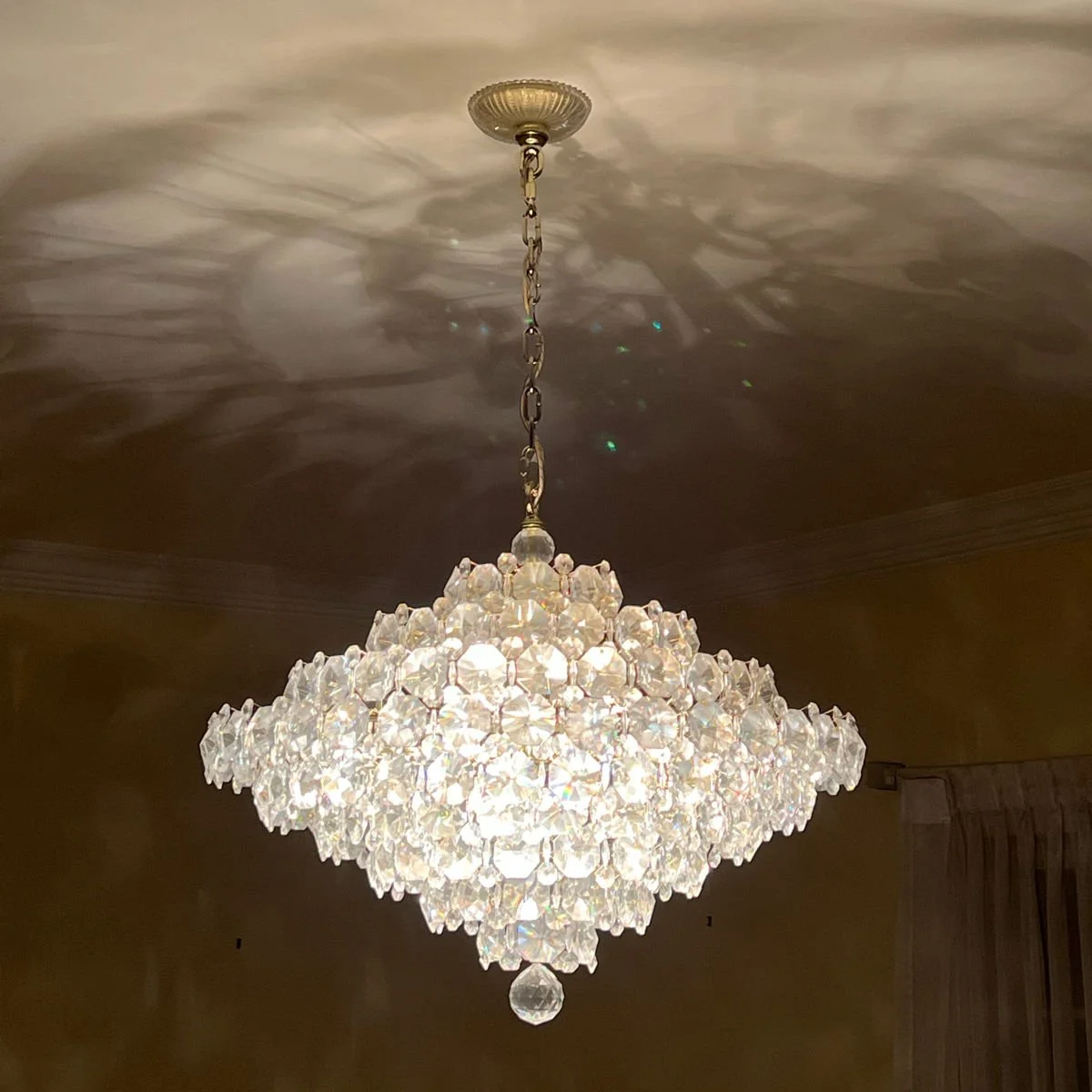 A large, elegant crystal chandelier hanging from a ceiling with a chain and a decorative ceiling mount, auctioned and photographed by ACES Gallery.