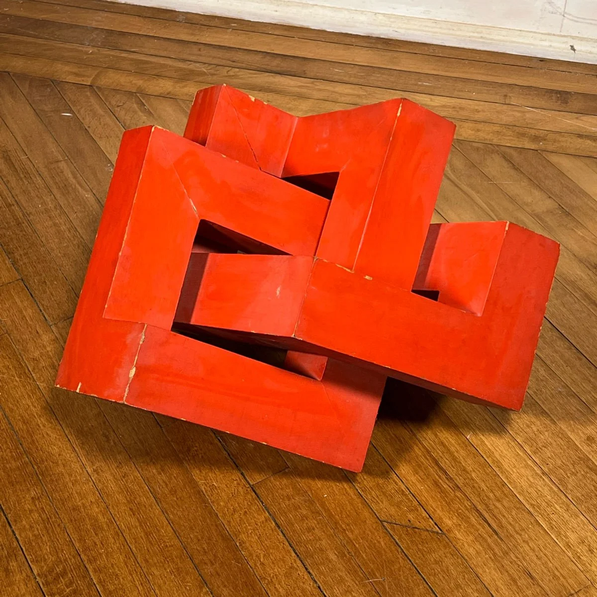 A red, geometric, sculptural piece of art on a wooden floor, auctioned and photographed by ACES Gallery.