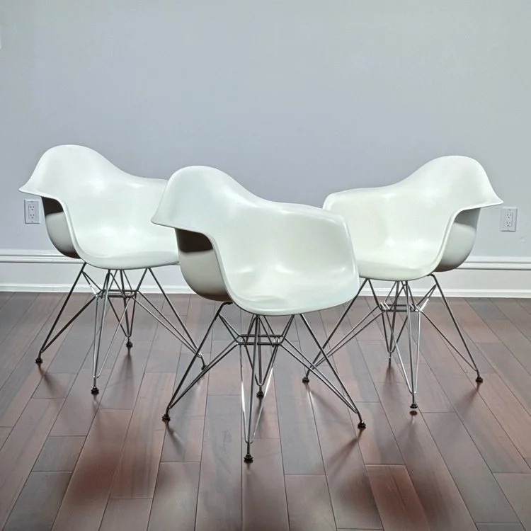 Three white modern chairs by Herman Miller with metal wire legs arranged in a circle in a room with hardwood floors and plain white walls, auctioned and photographed by ACES Gallery.