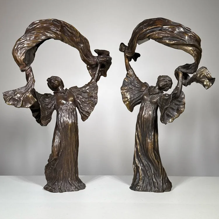 Two bronze sculptures of women in flowing dresses holding large, flowing fabric above their heads, displayed against a plain light gray background, auctioned and photographed by ACES Gallery.