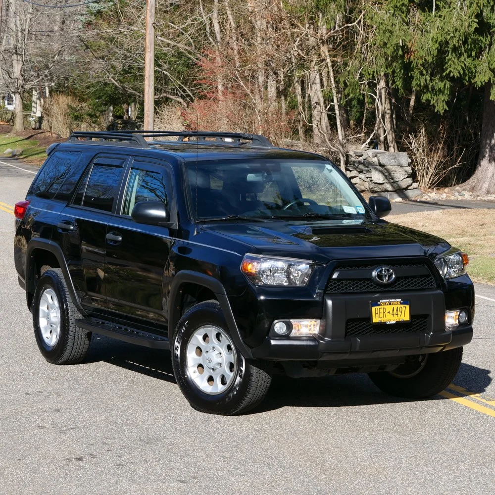 A black Toyota 4Runner SUV parked on a street with trees and rocks in the background, auctioned and photographed by ACES Gallery.