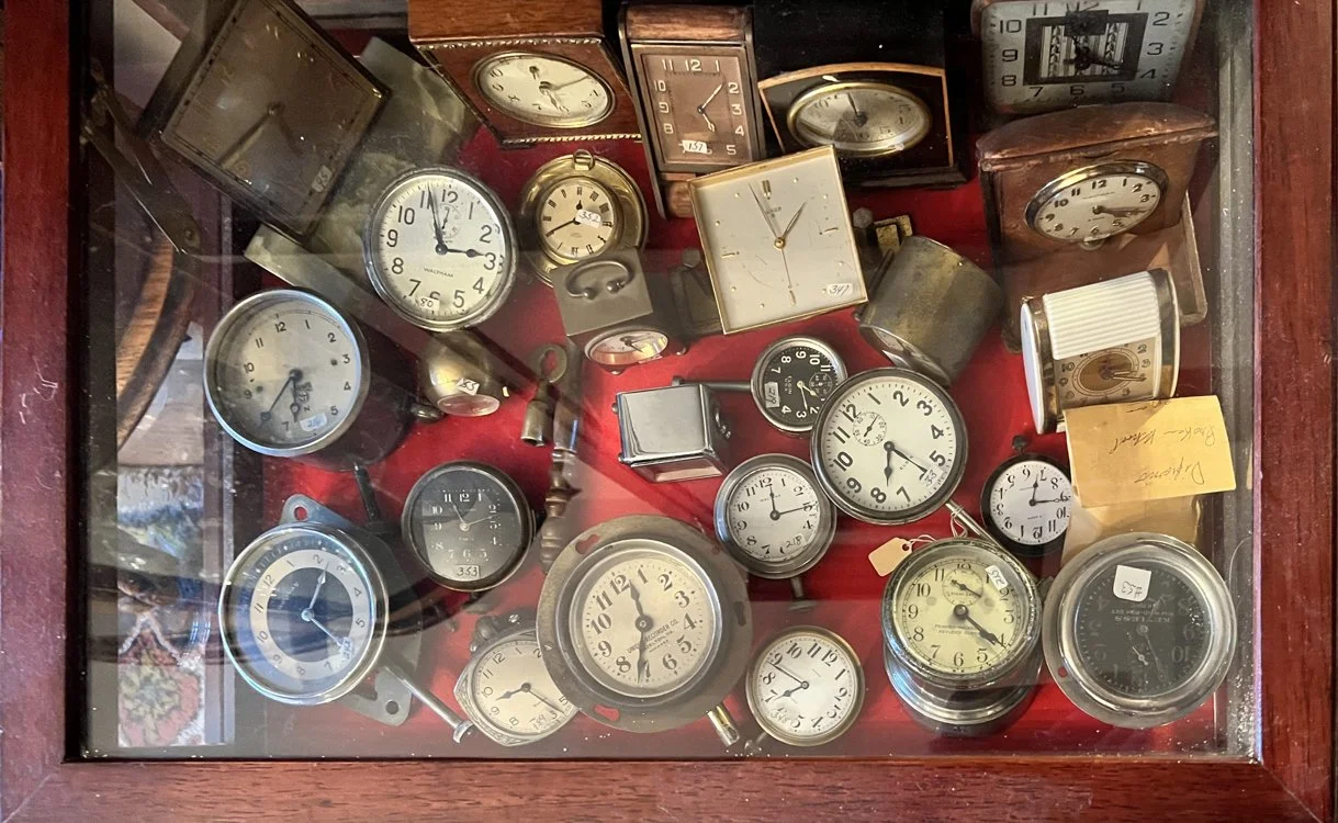 Collection of vintage clocks and timepieces arranged under glass in a wooden display case, auctioned and photographed by ACES Gallery.
