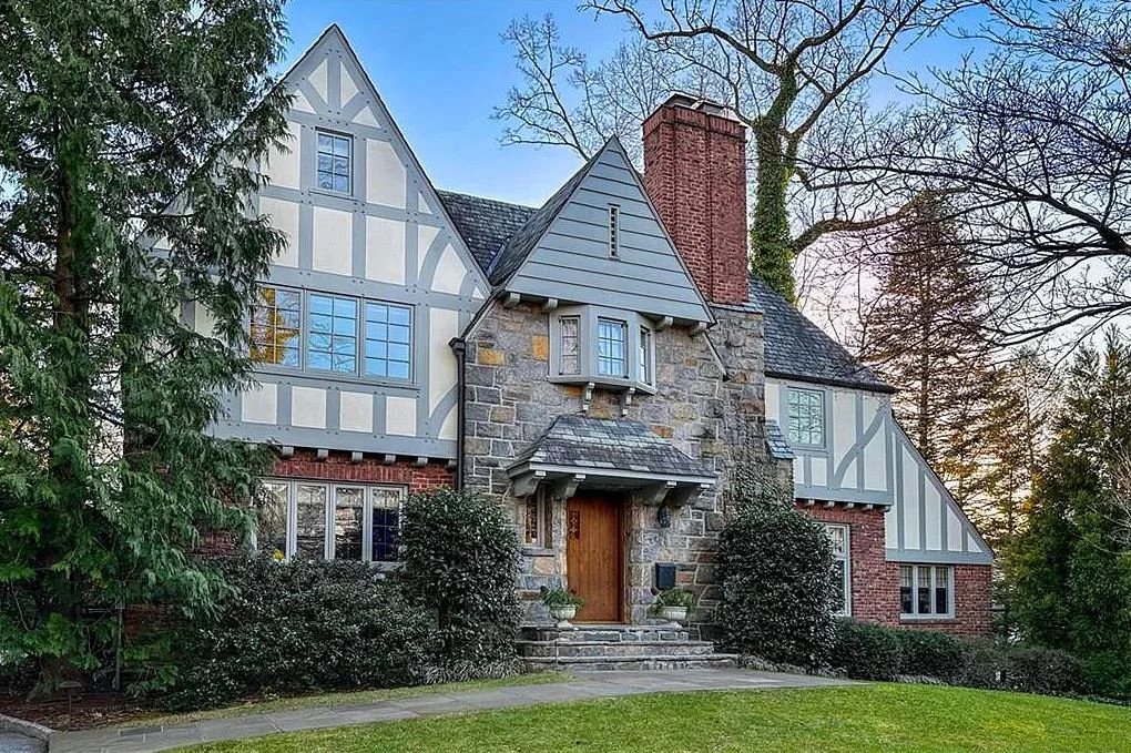 A large historic house with Tudor-style architecture, featuring stone and half-timbered walls, a steeply pitched roof, and multiple chimneys, set amidst trees and a manicured lawn, representing an ACES estate client.