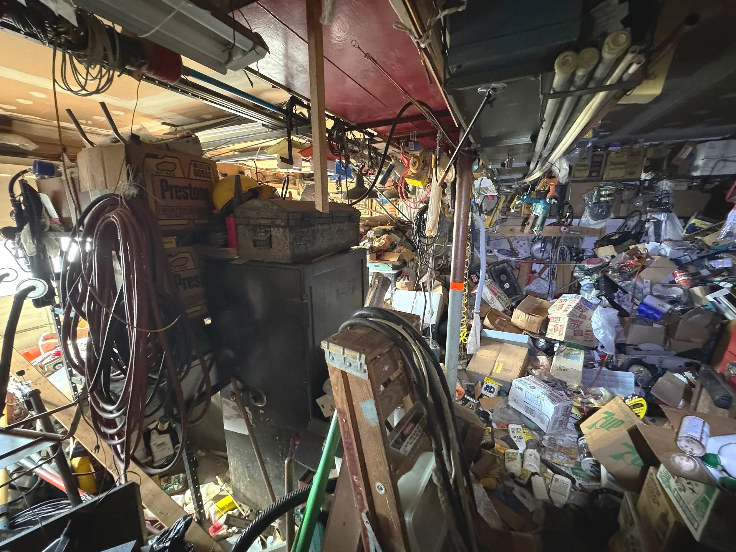 A cluttered workshop or storage room with various tools, boxes, wires, and equipment scattered around.