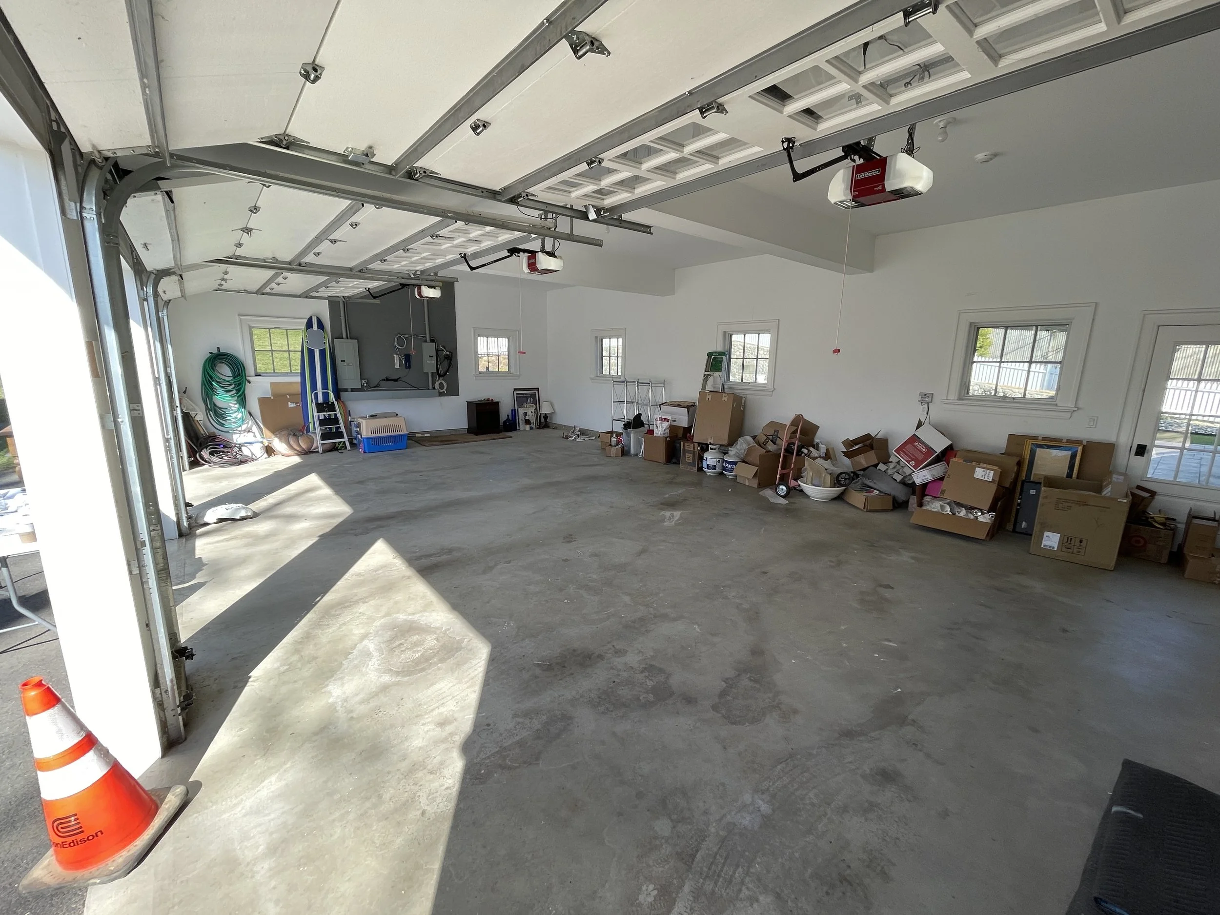Empty garage with a open door, scattered boxes, and tools along the walls, sunlight casting shadows on the concrete floor, emptied following an estate auction and cleanout project by ACES.