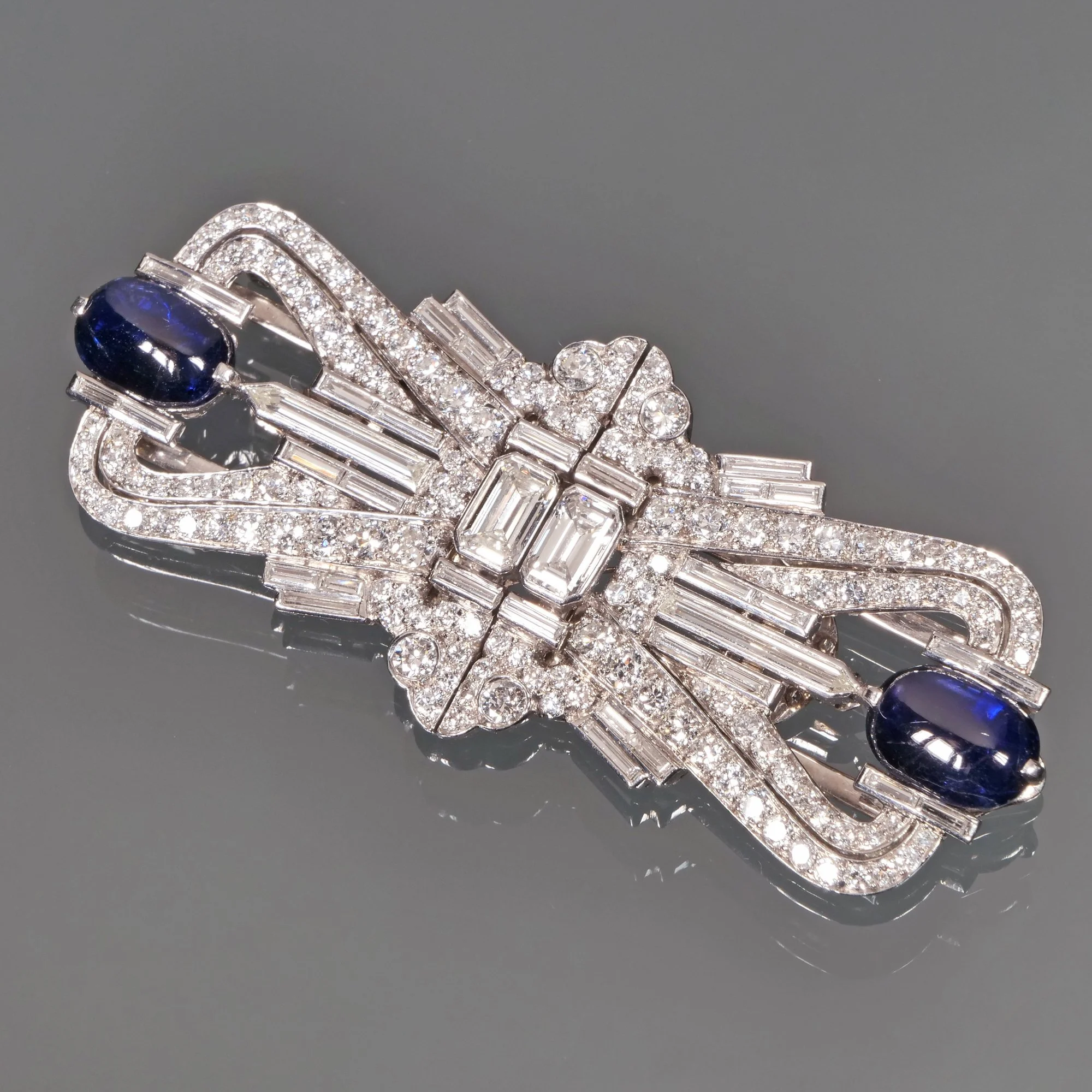 An ornate silver brooch decorated with diamonds and two blue cabochon gemstones.
